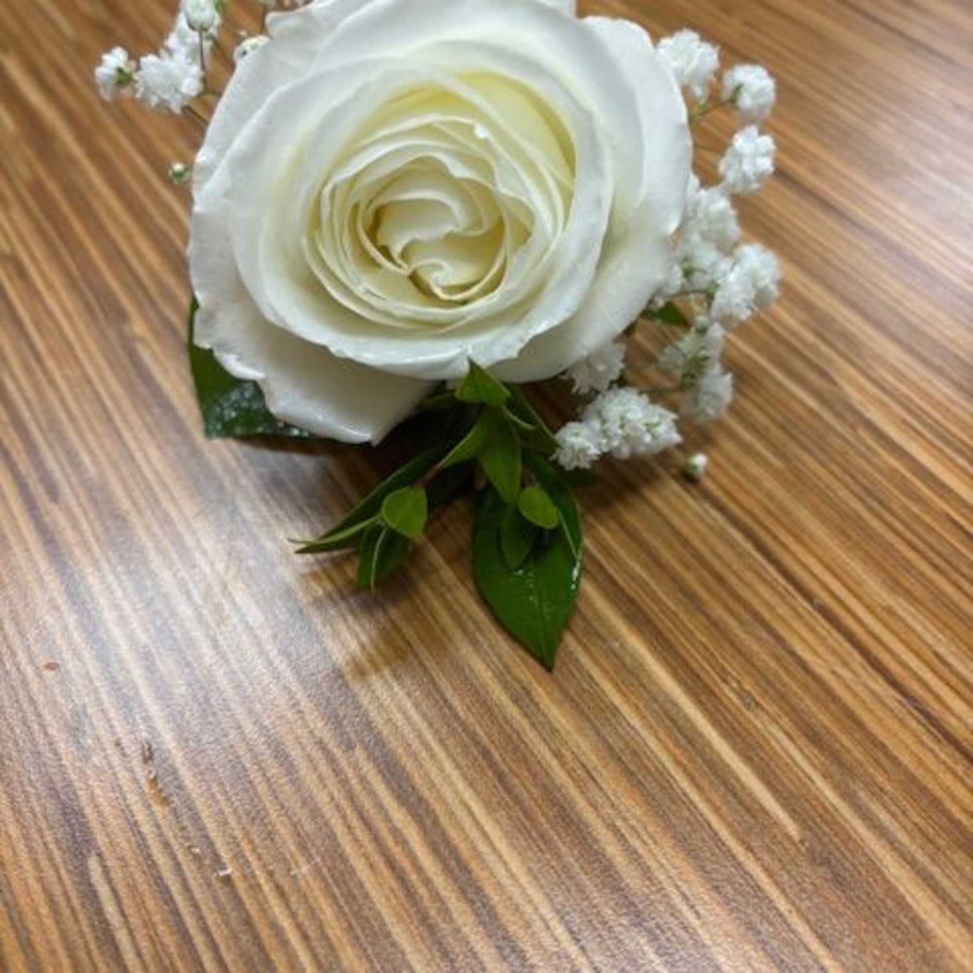 White rose boutonniere with baby's breath on a wooden surface