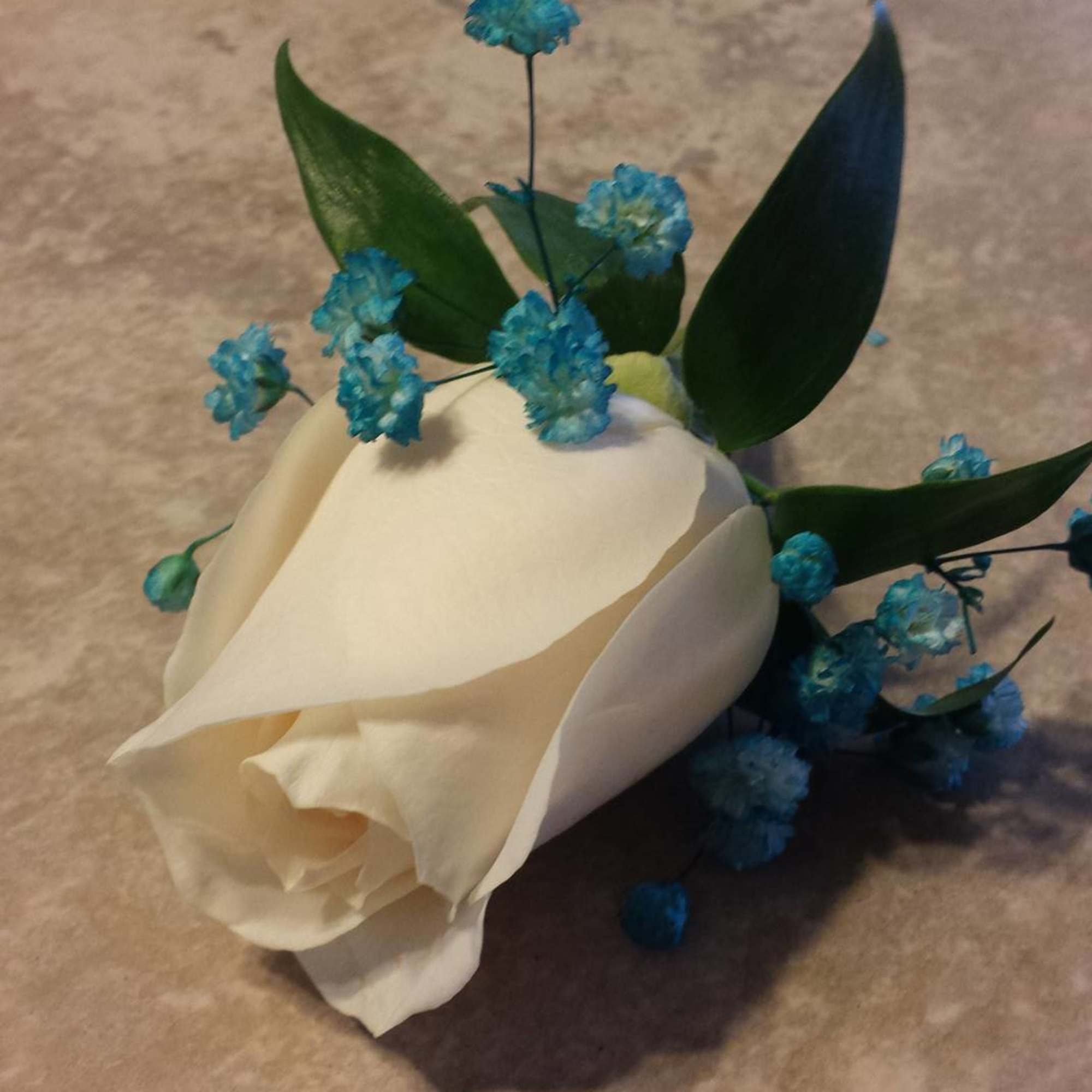 White rose boutonniere with blue filler flowers and green leaves