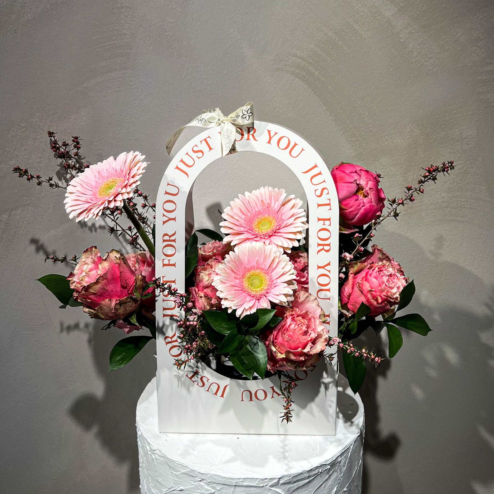 Pink gerbera daisies and roses arranged in a white gift bag with a ribbon handle.