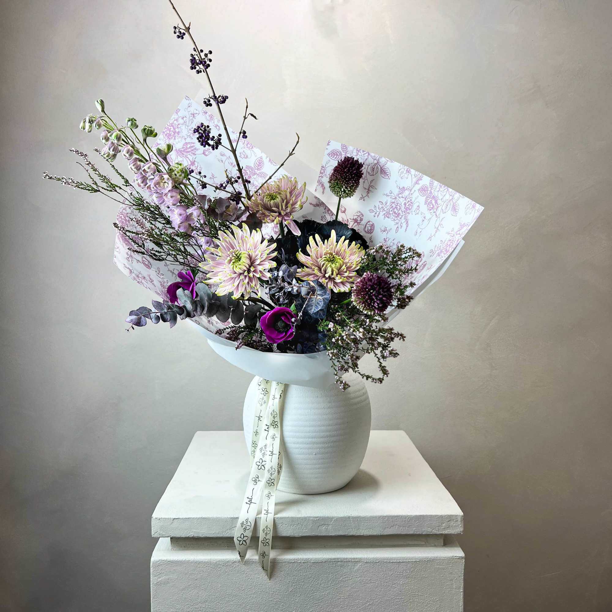 Mixed bouquet of purple and pale pink flowers in a white vase
