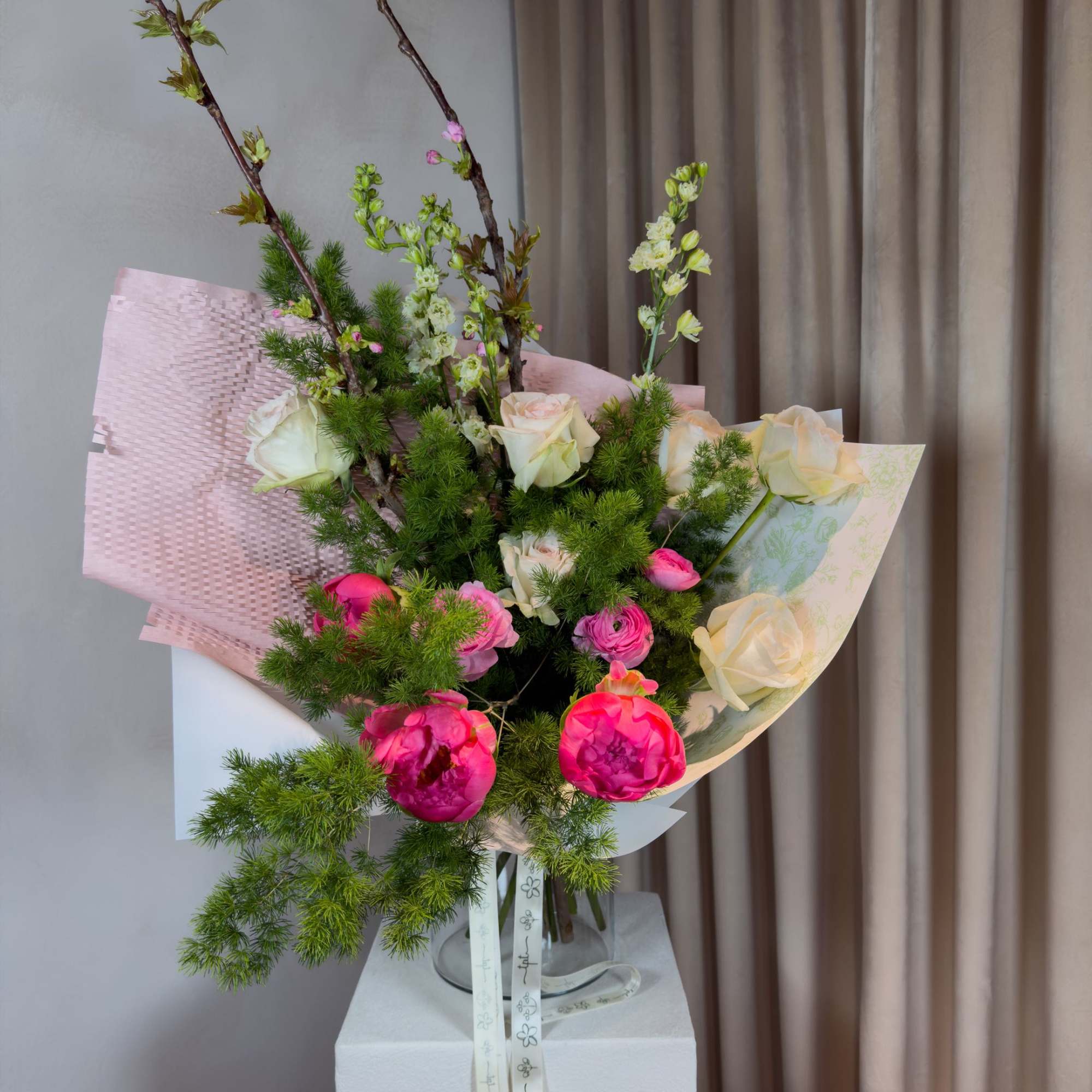 Tall bouquet of pink and white roses with branching blossoms in pastel wrap