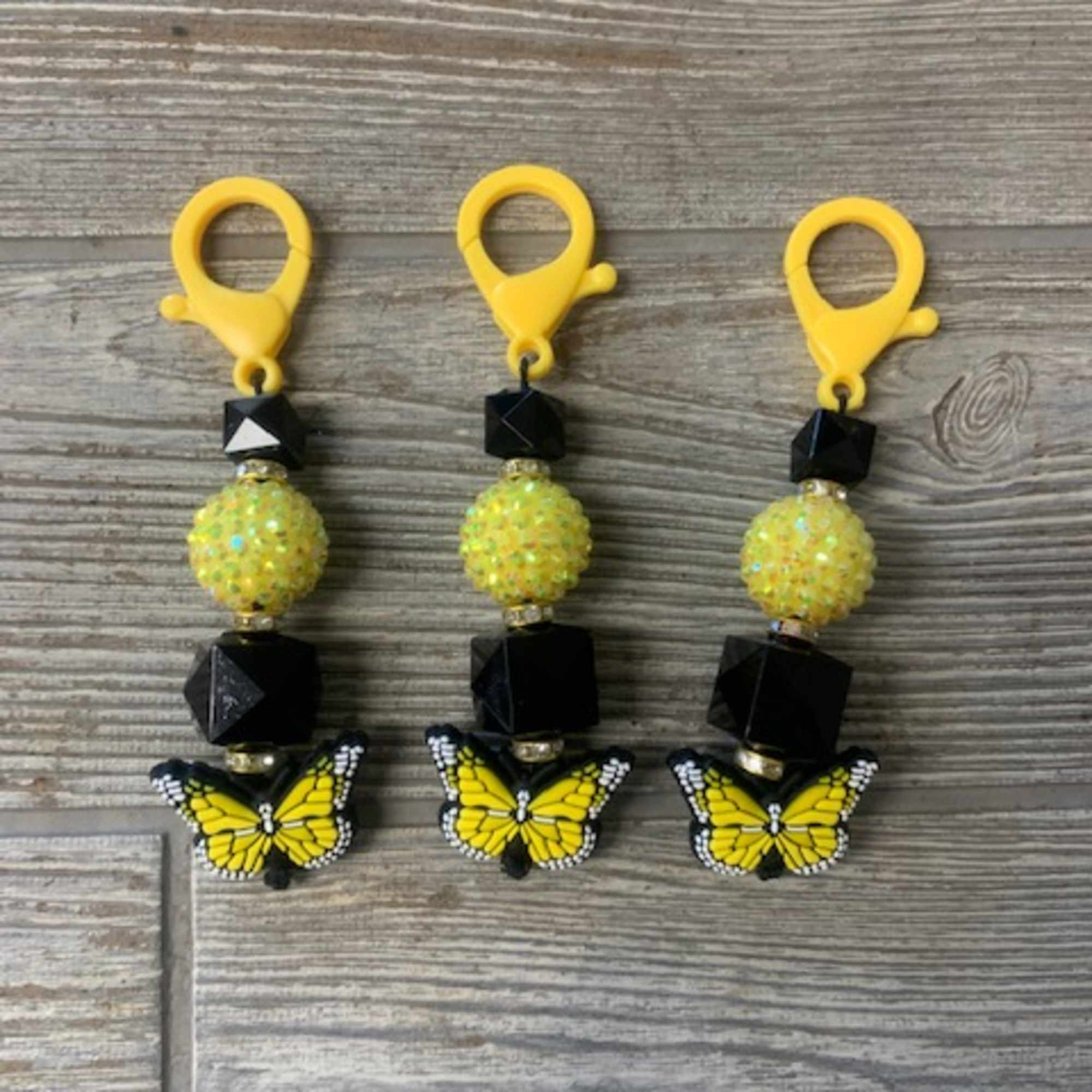 Three butterfly bead charms with yellow clips on a wood surface