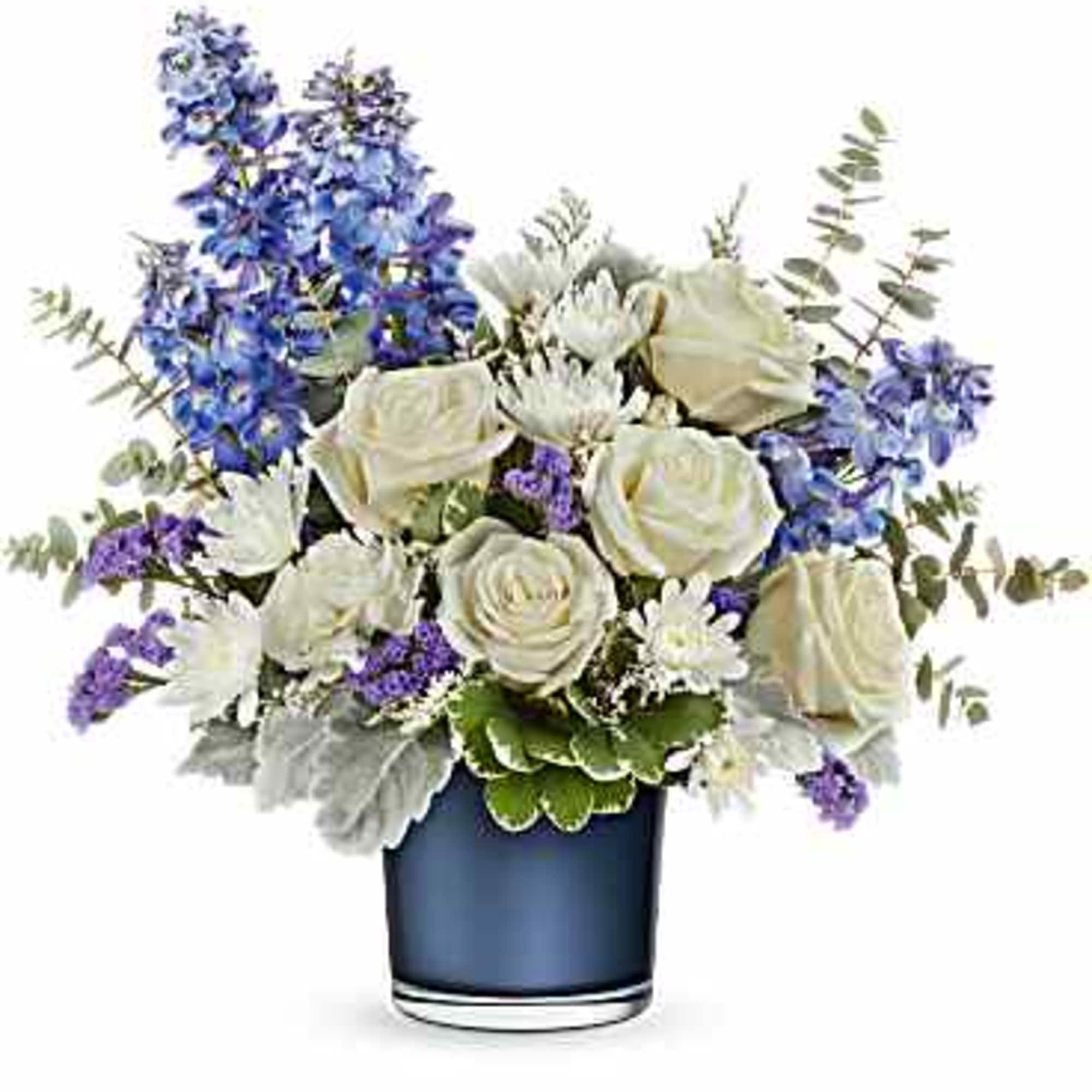 White roses and blue delphinium with purple accents arranged in a navy glass cylinder vase