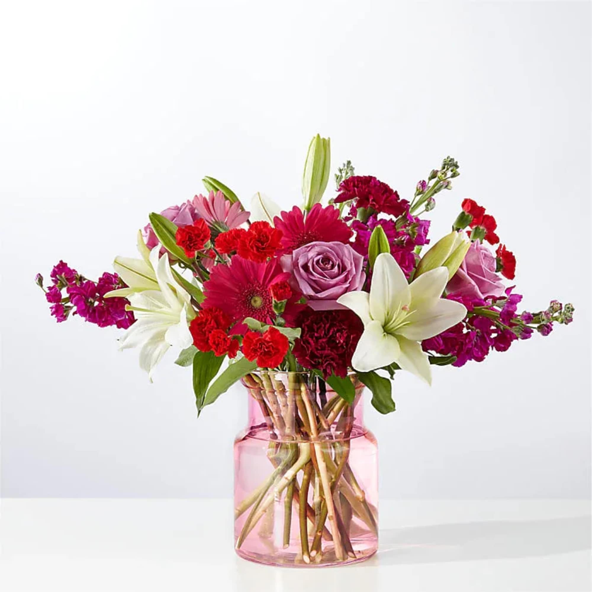 Mixed bouquet of pink, red, and white flowers in a pink glass vase