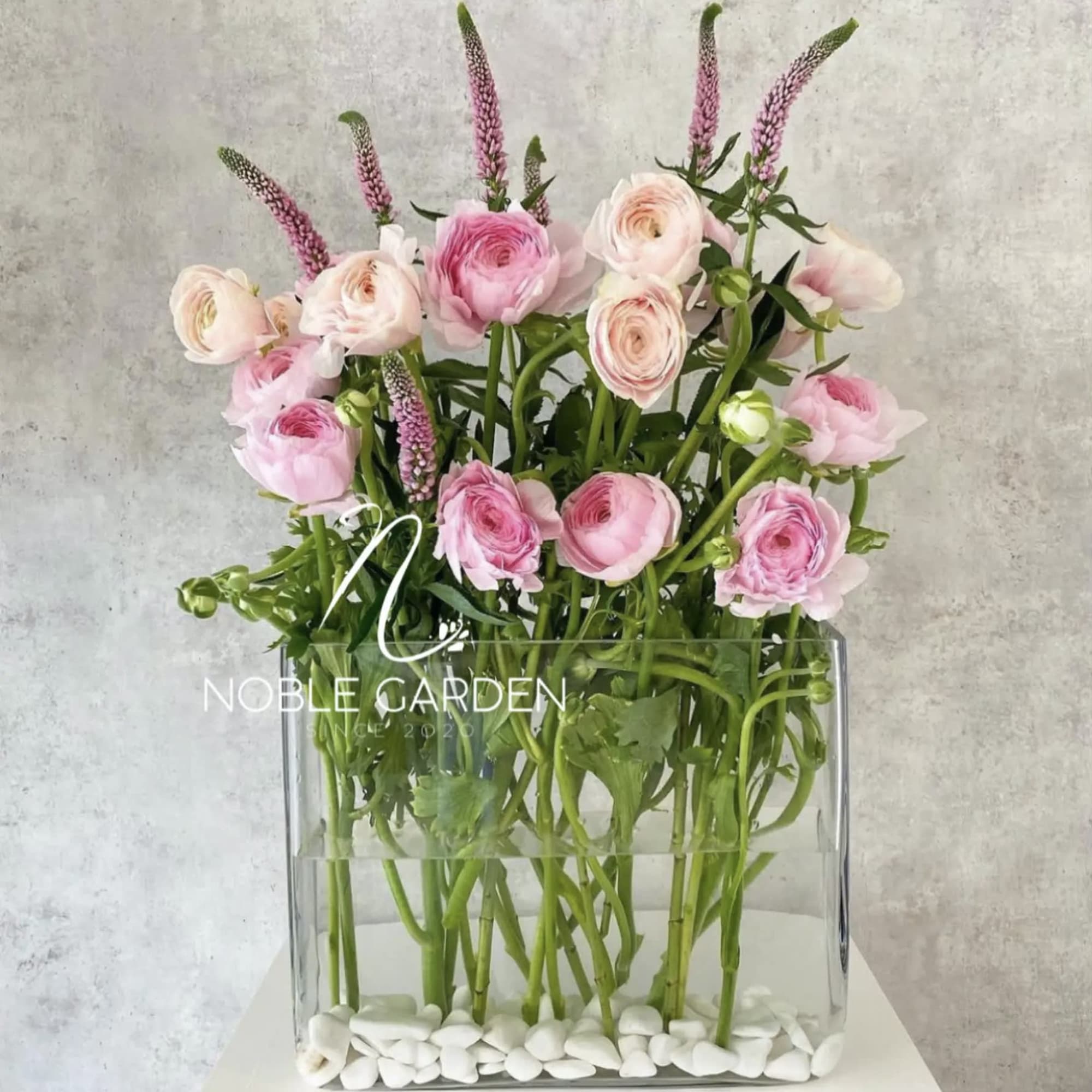 Pink ranunculus and pale roses in a clear rectangular vase