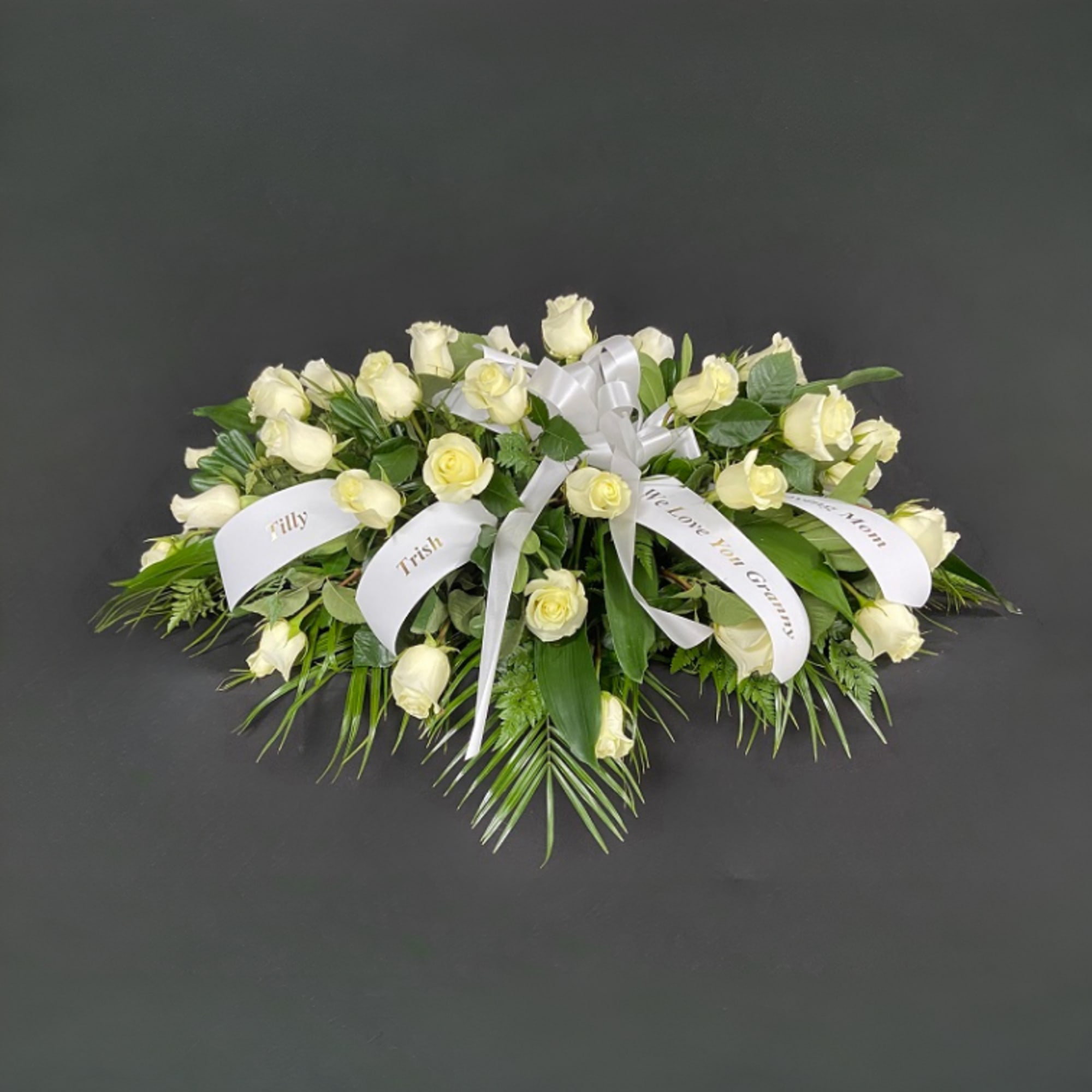 White rose funeral spray with ribbon names on a dark background