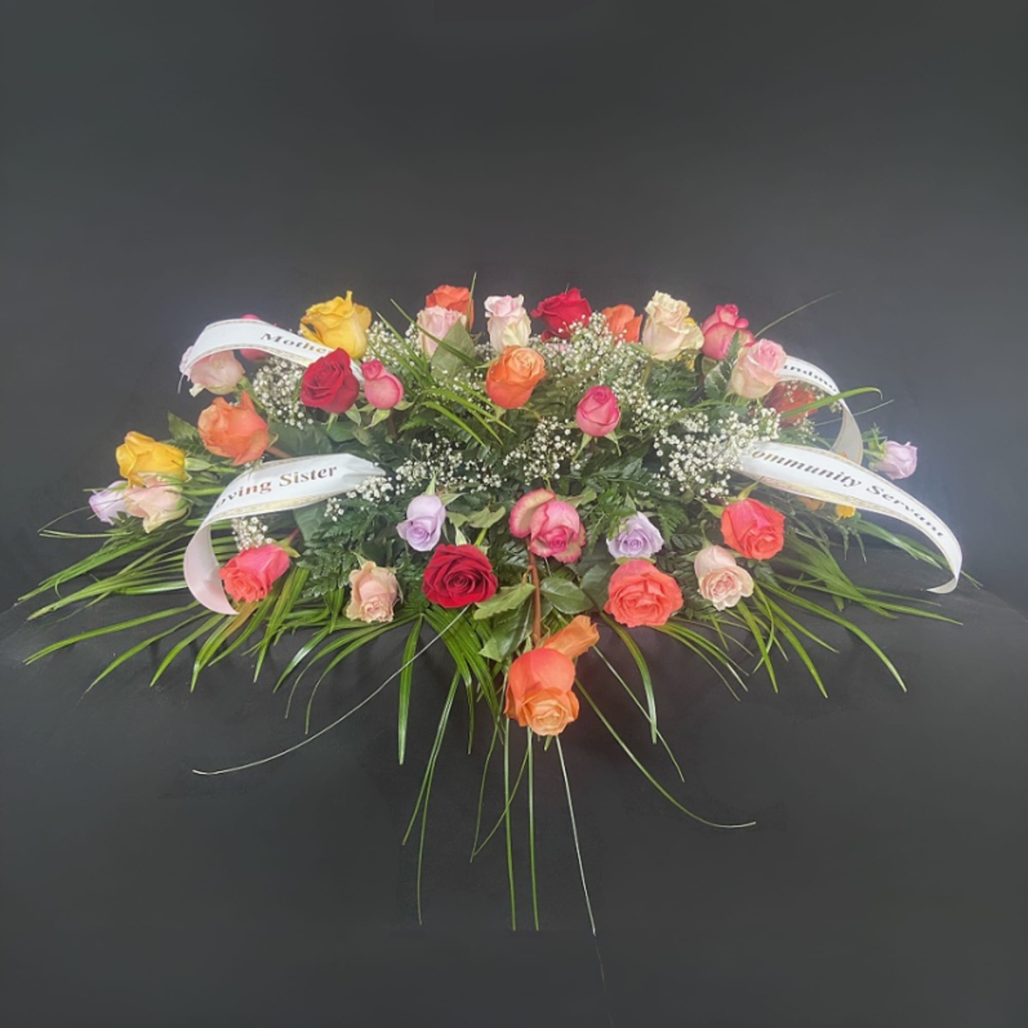 Flat floral spray of multicolored roses with white ribbon