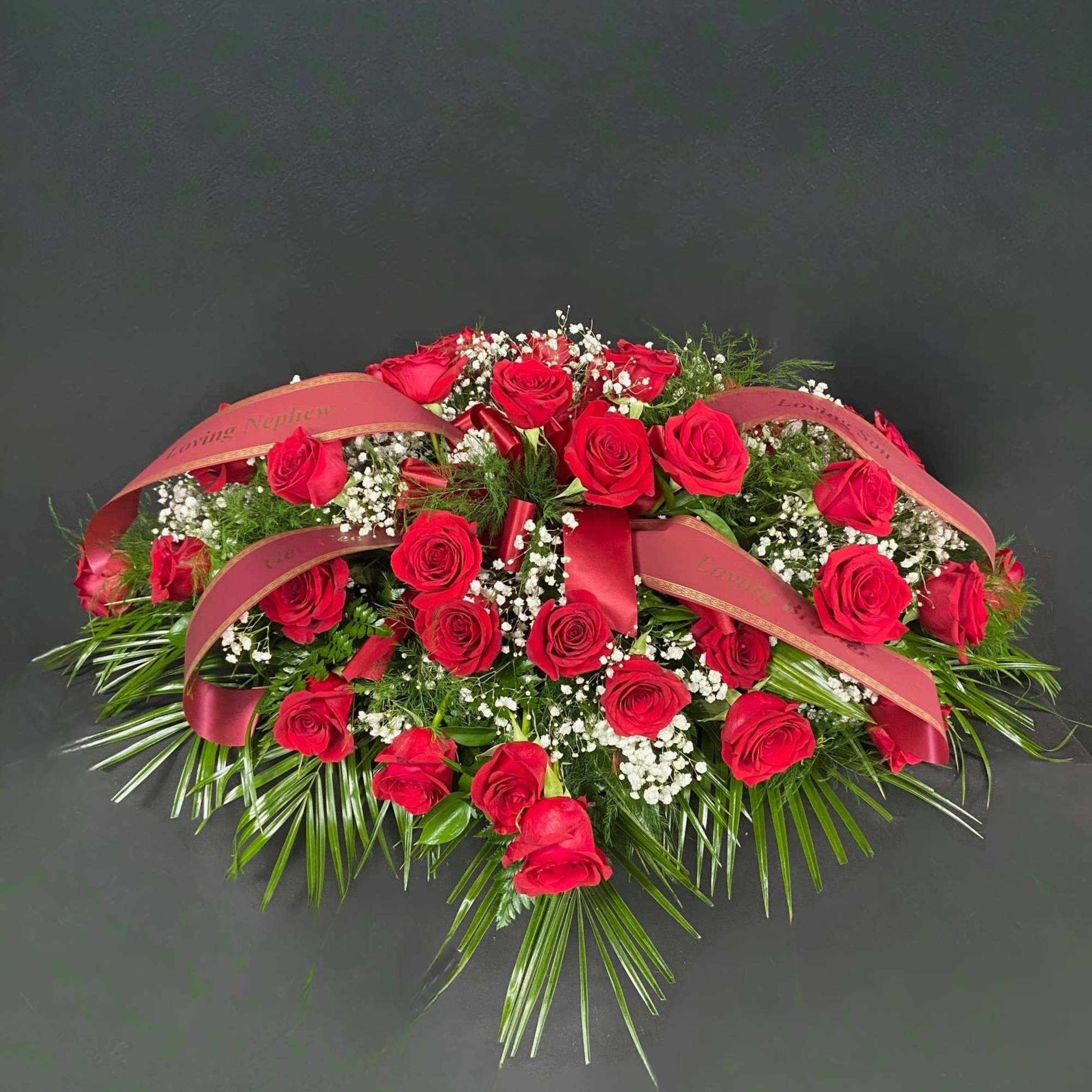 Red roses arranged with baby's breath and ribbon on a dark background