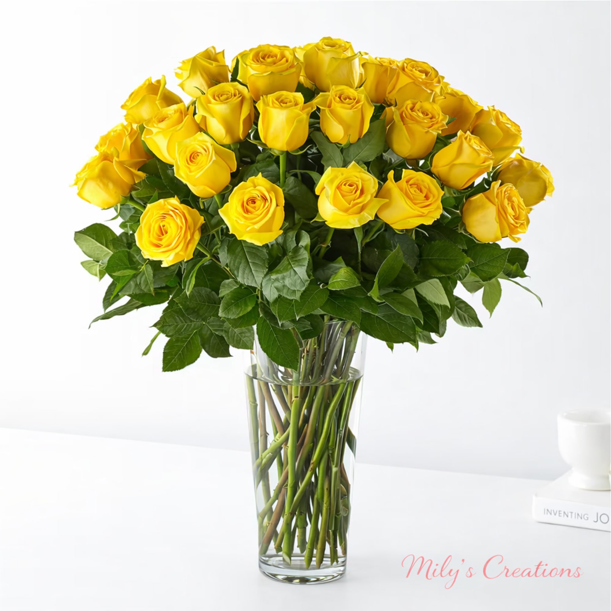 Tall clear vase filled with a large bouquet of bright yellow roses against a white background