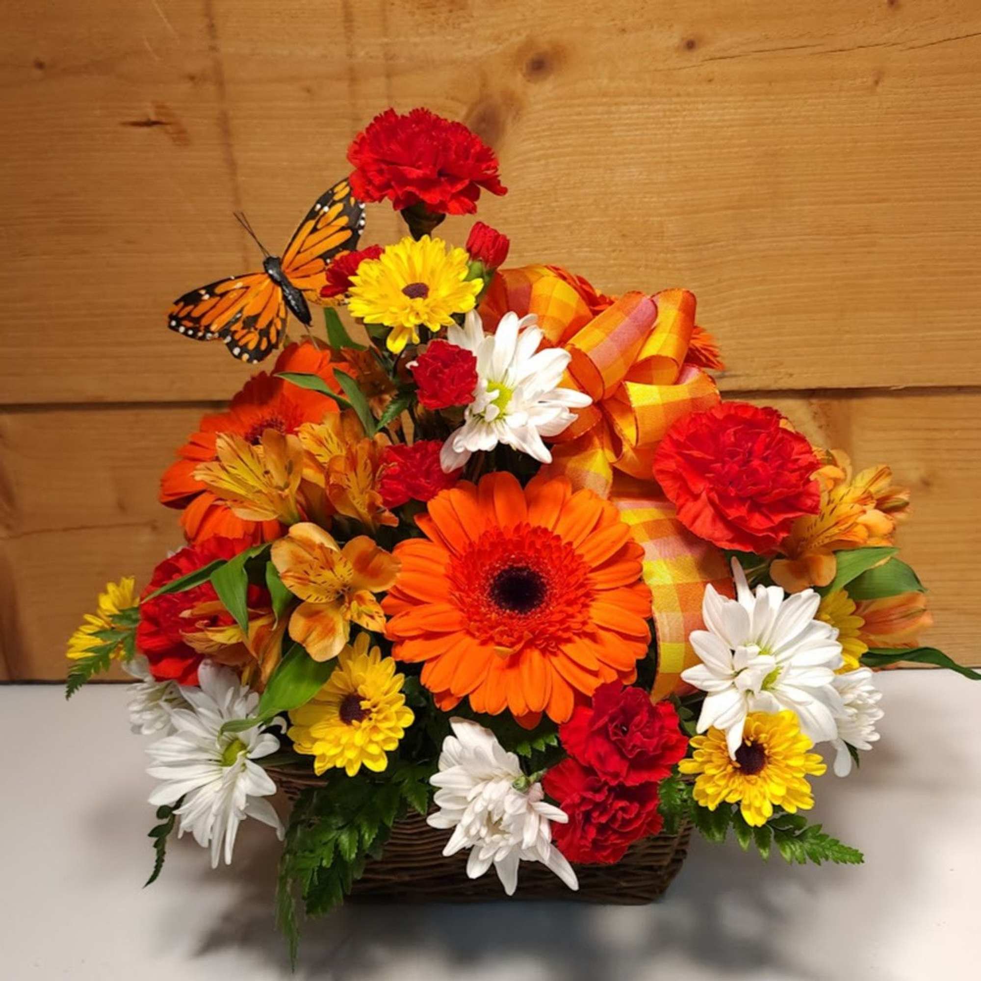 Autumn floral basket with orange, red, yellow, and white blooms and a butterfly accent