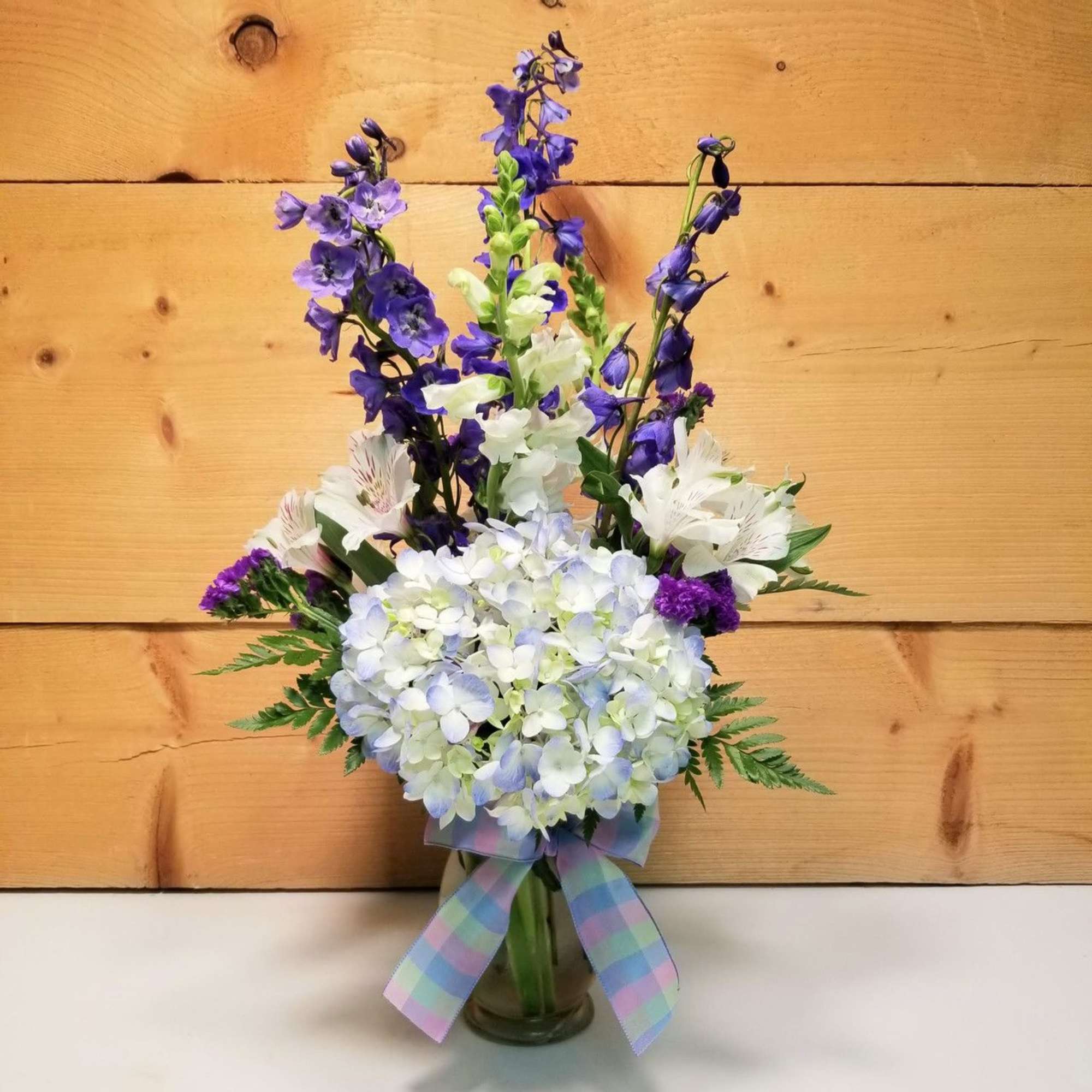 Purple and white flowers arranged in a glass vase with a plaid ribbon.
