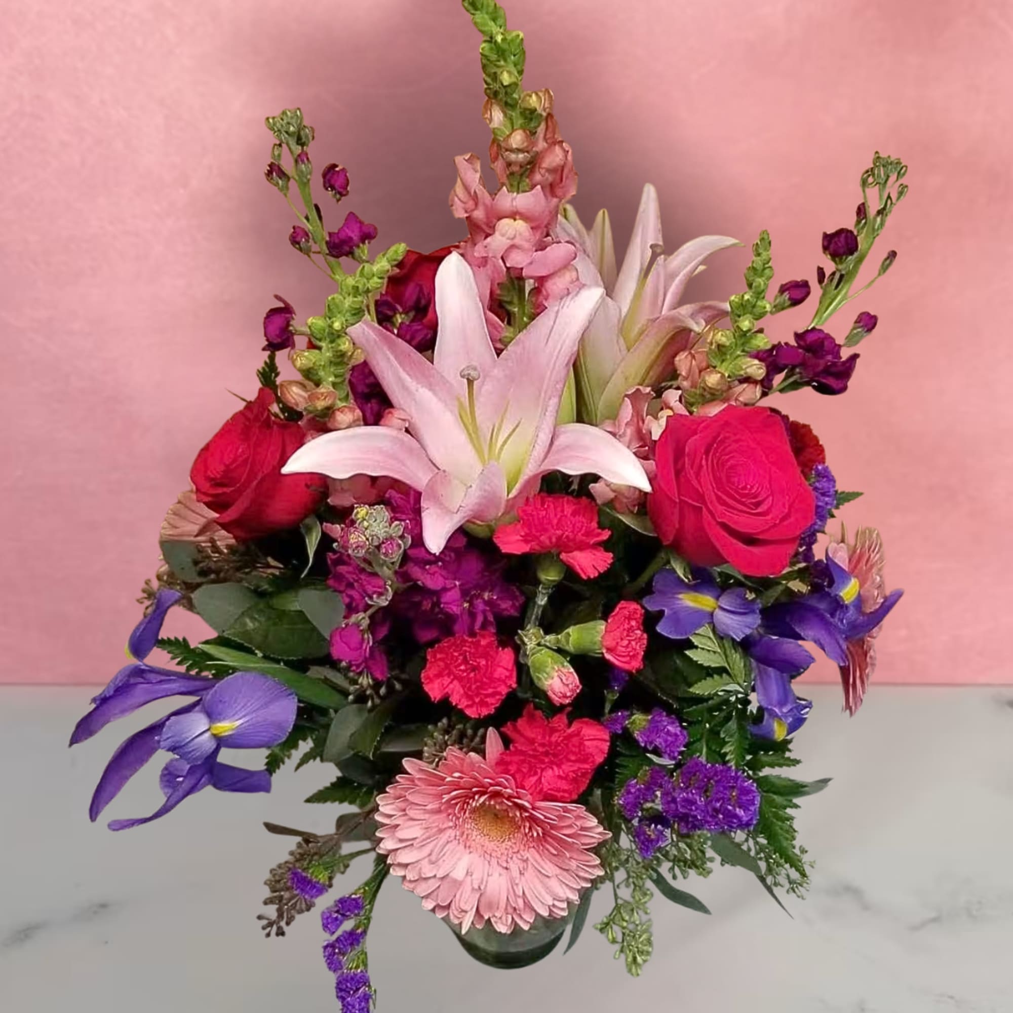 Mixed bouquet with pink lilies, roses, and purple flowers in a glass vase