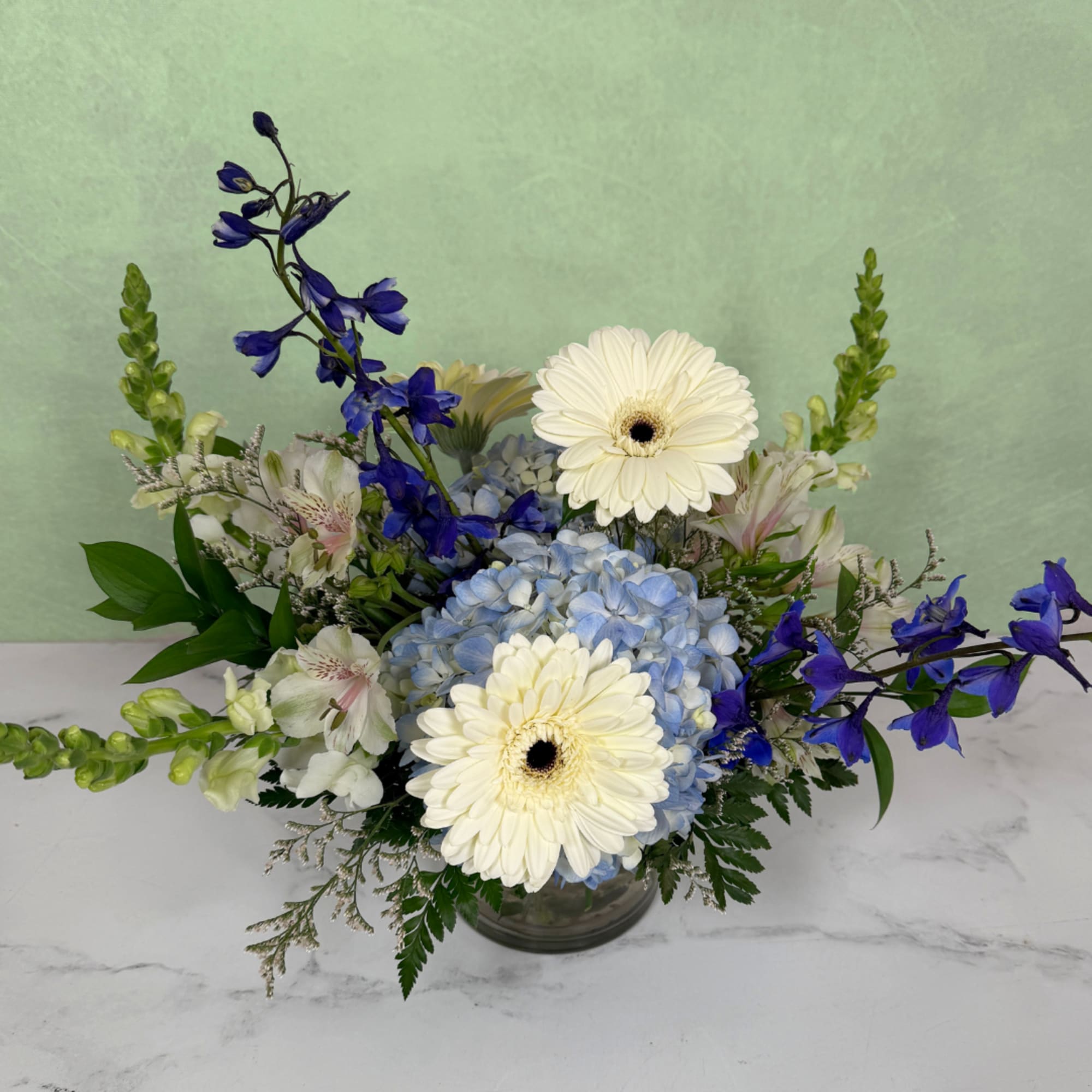 Blue hydrangeas with white gerbera daisies and blue flowers in a glass vase
