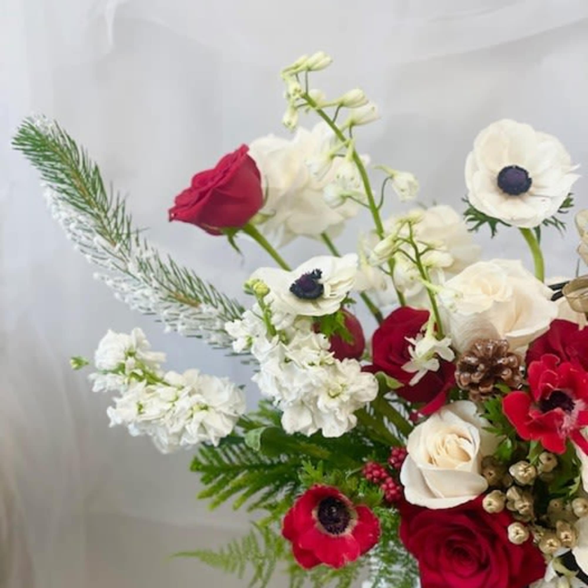 Red and white floral arrangement with anemones and roses in a dark vase