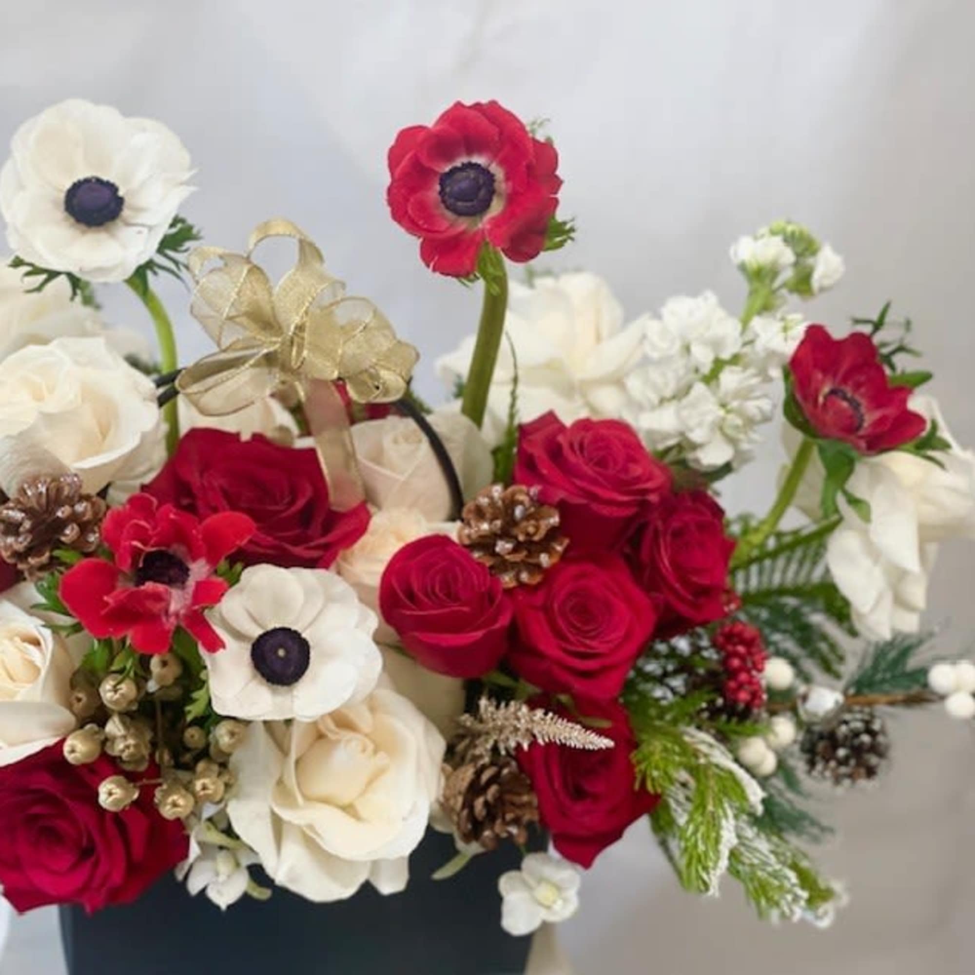 Bouquet of red and white flowers with pinecones and a gold ribbon