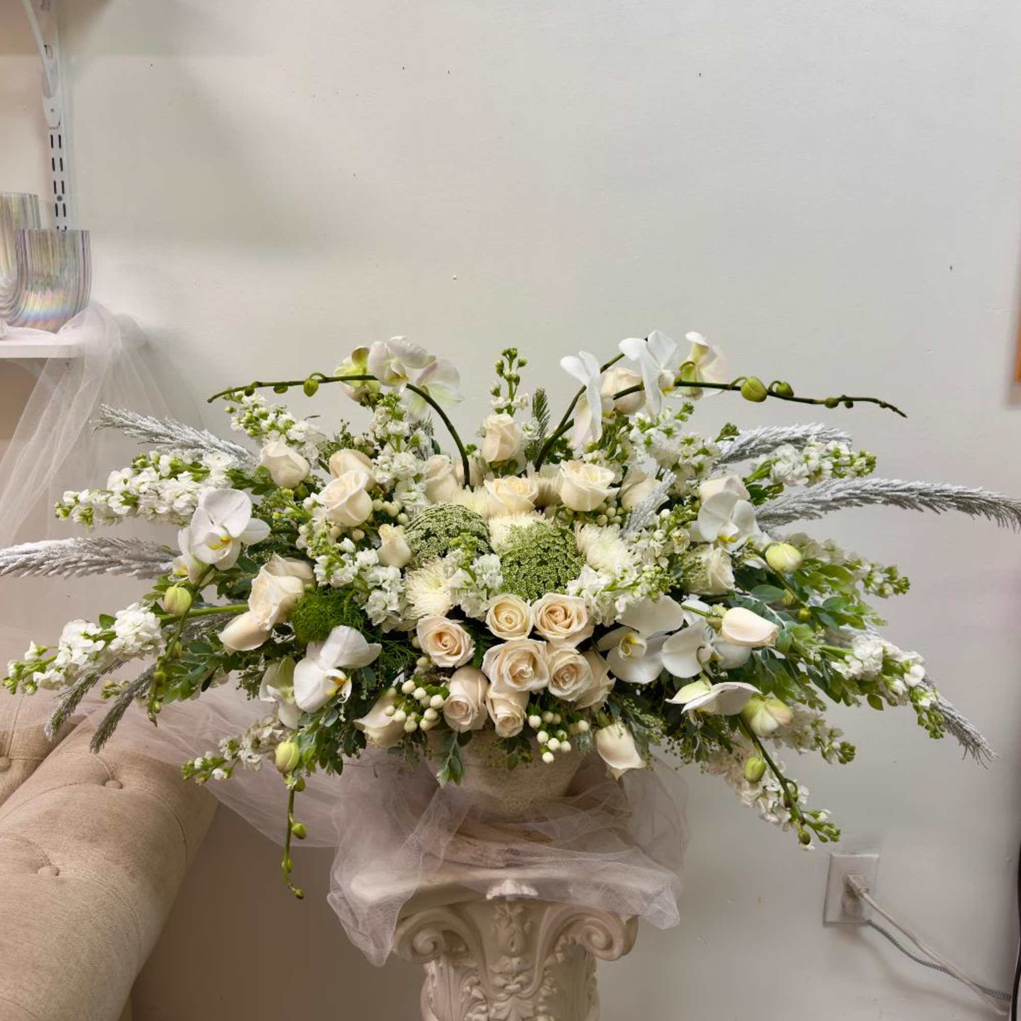 Large white floral arrangement with roses and orchids in a pedestal vase
