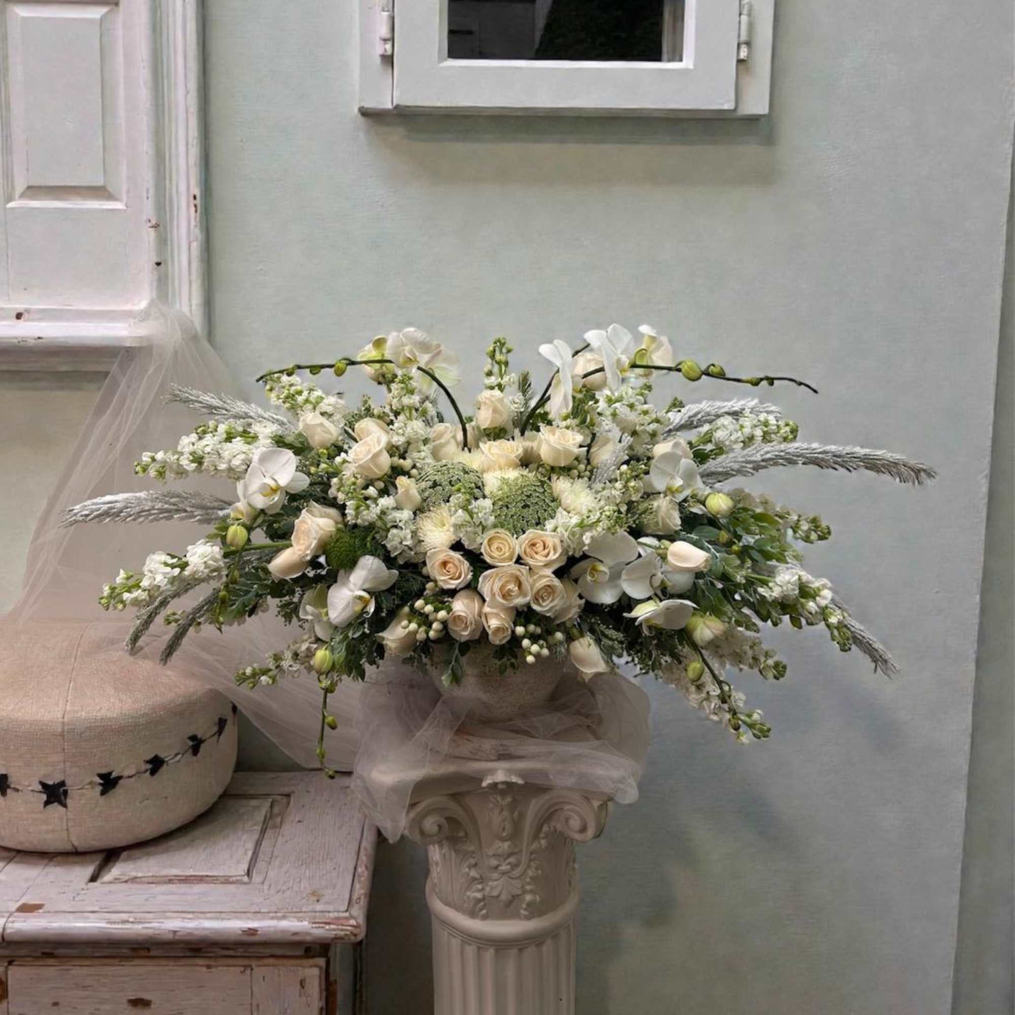 Large white floral arrangement on a pedestal with roses and orchids