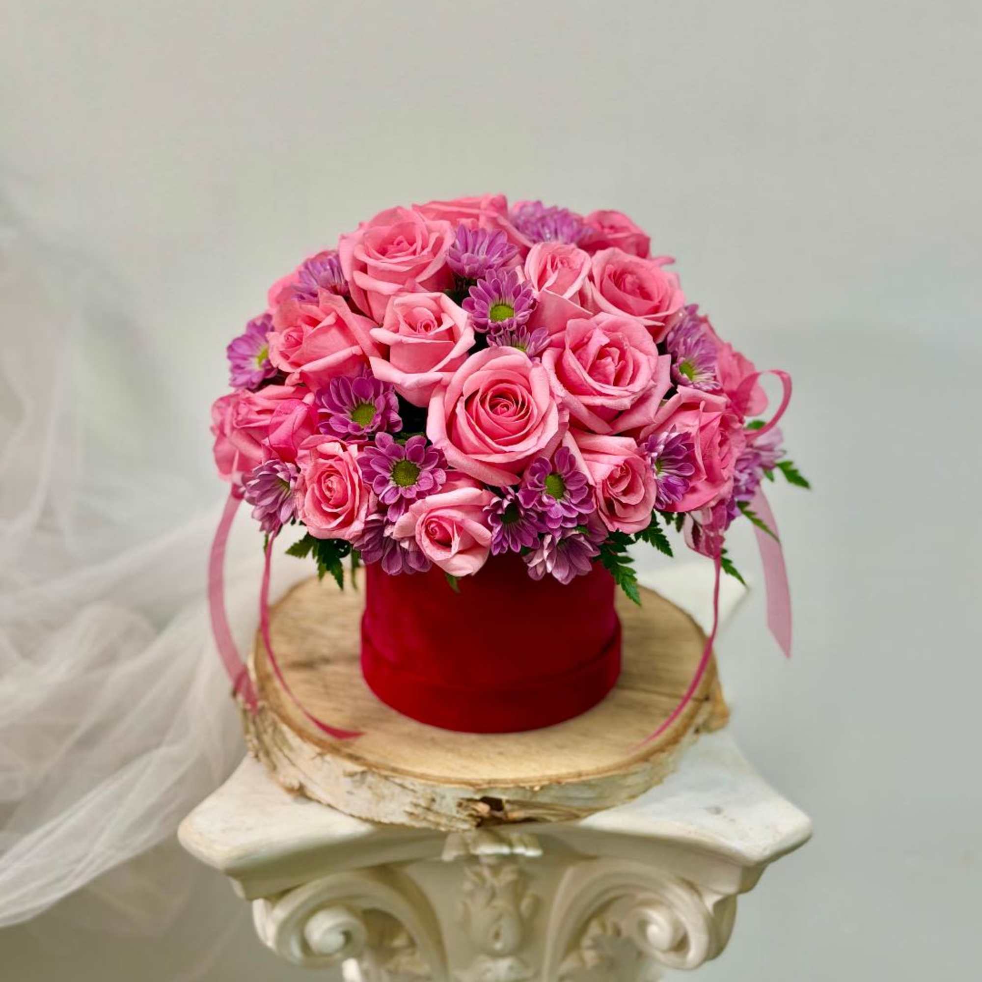 Pink roses and purple daisies arranged in a red box