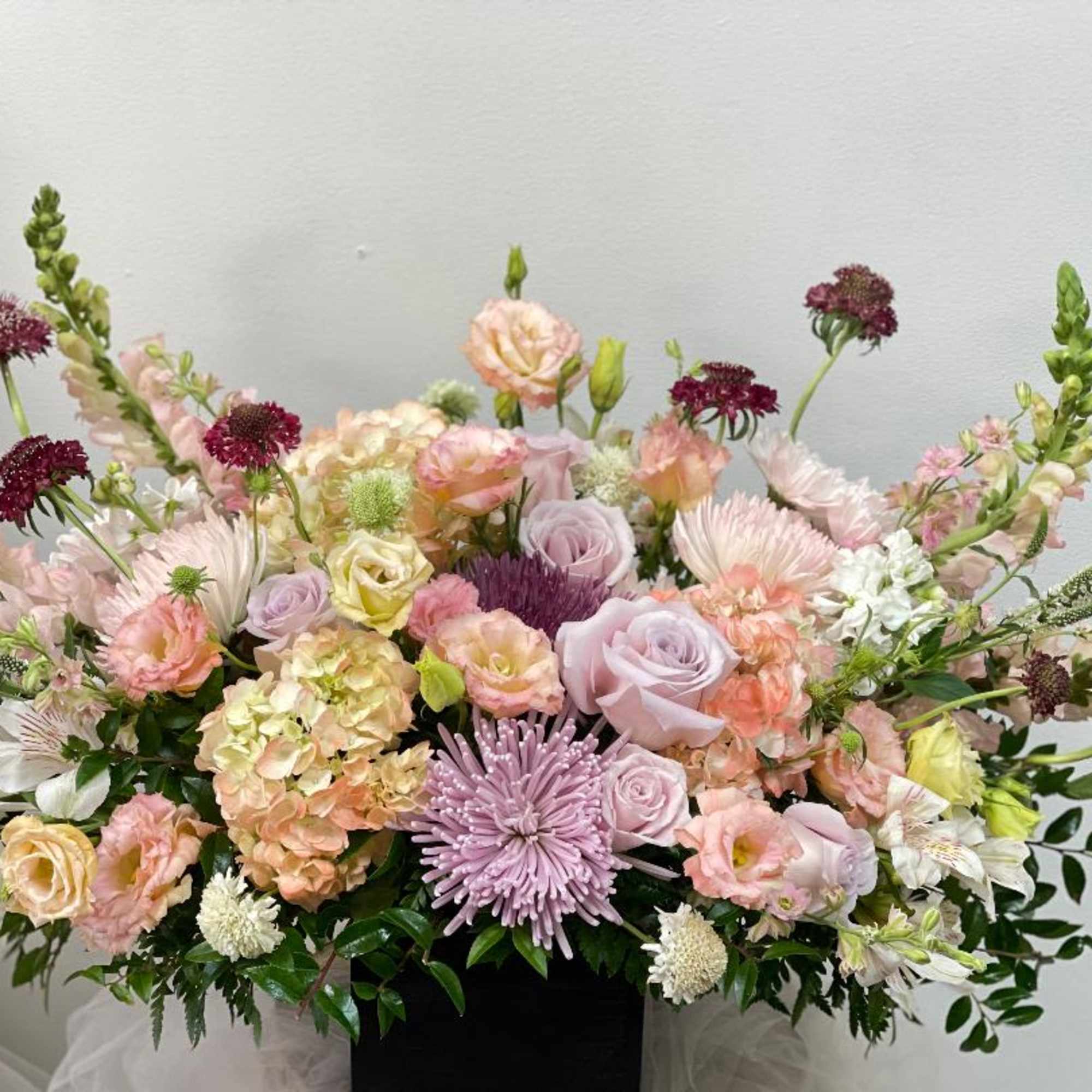 Large pastel floral arrangement with roses, hydrangeas, and chrysanthemums in a black container