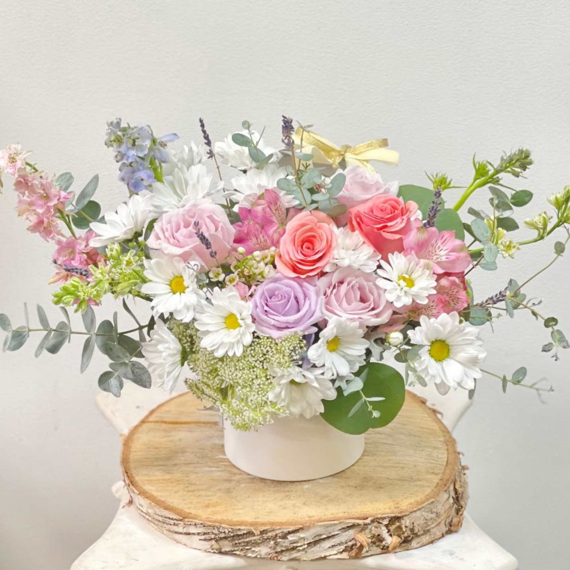Pastel bouquet of roses and daisies in a white container