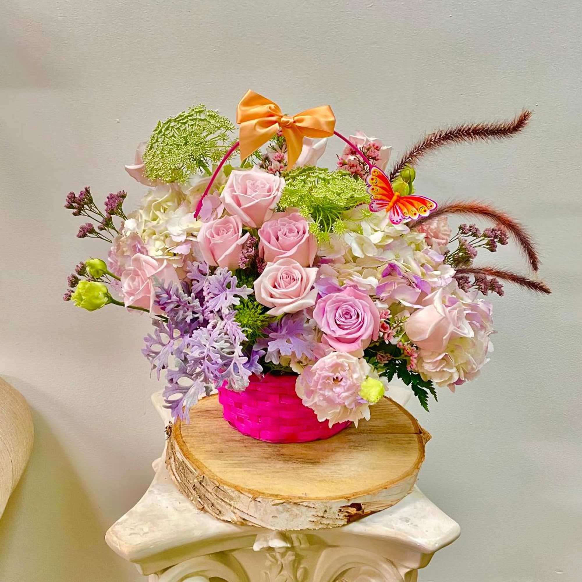 Pink roses and pastel flowers in a bright pink basket with a bow