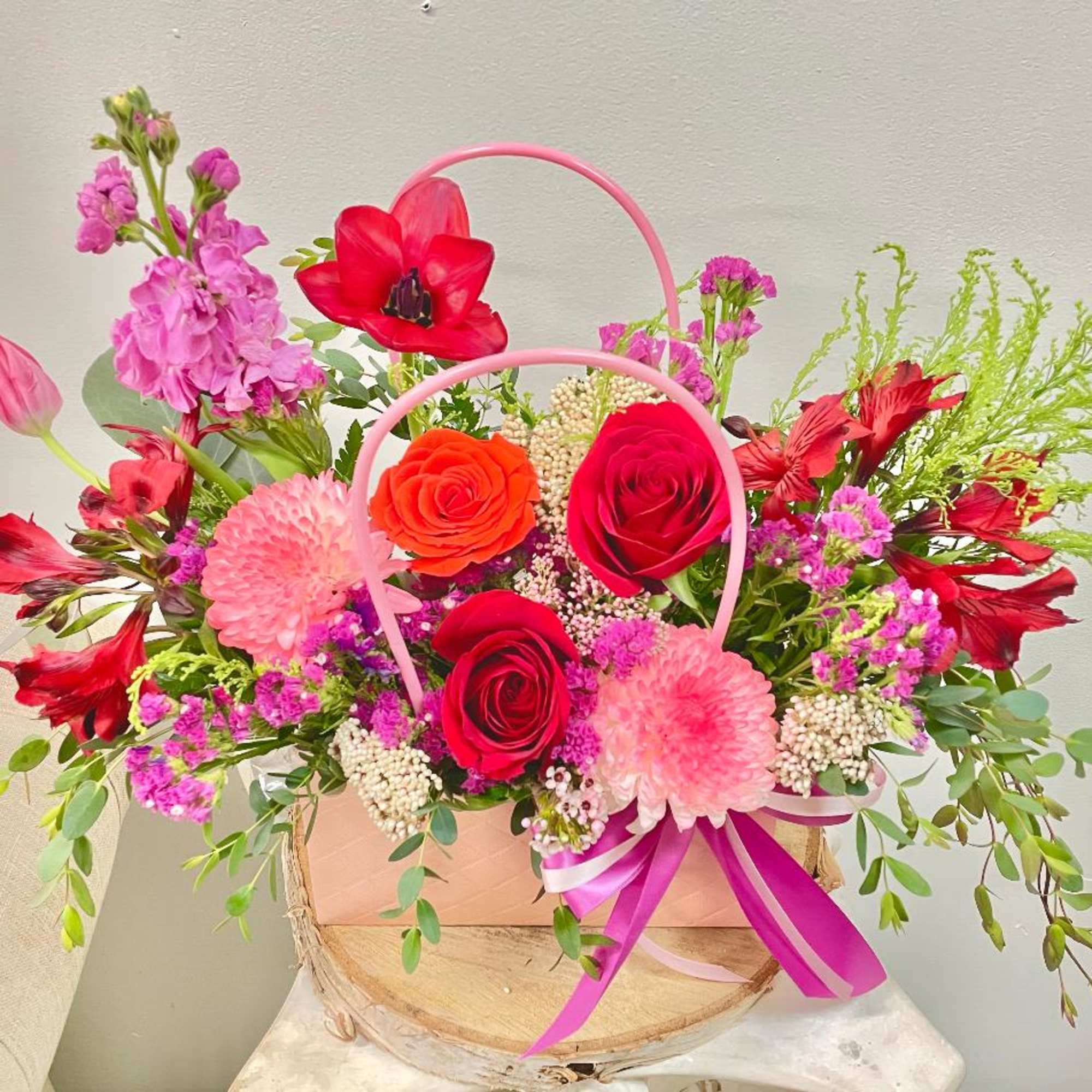 Pink and red flower arrangement in a basket with ribbon handles