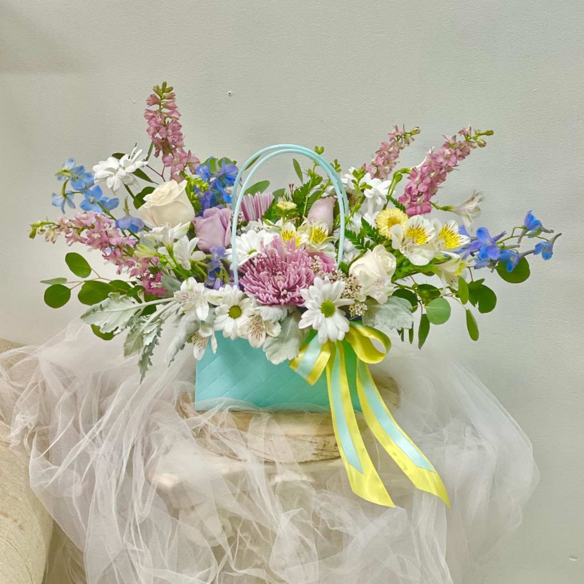 Pastel mixed flower arrangement in a turquoise basket with ribbon