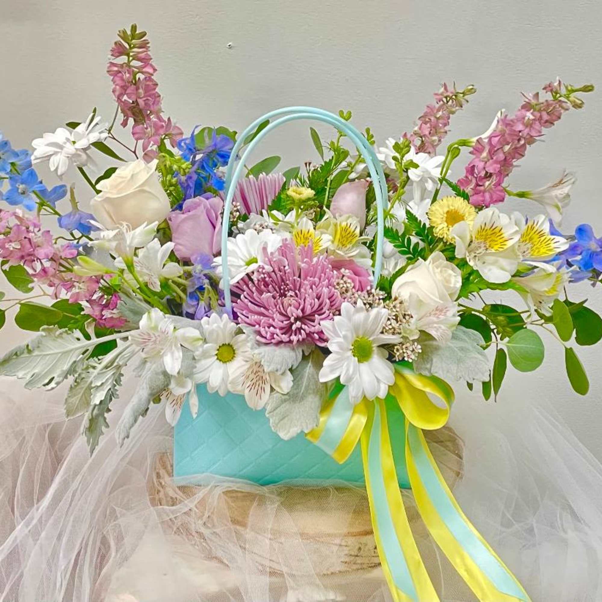 Colorful mixed flower arrangement in a turquoise basket with ribbon