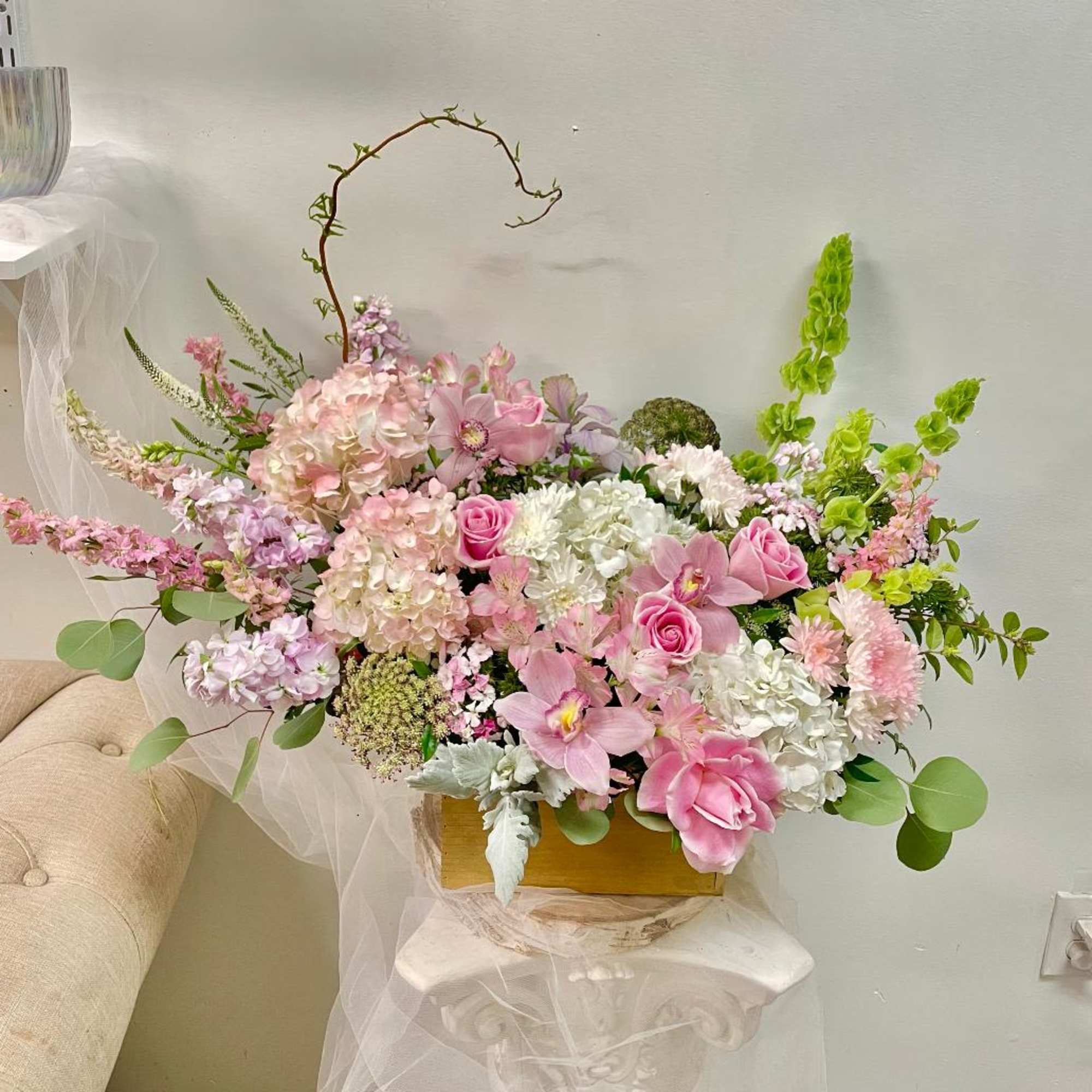 Pink and white floral arrangement in a gold box with arching branches