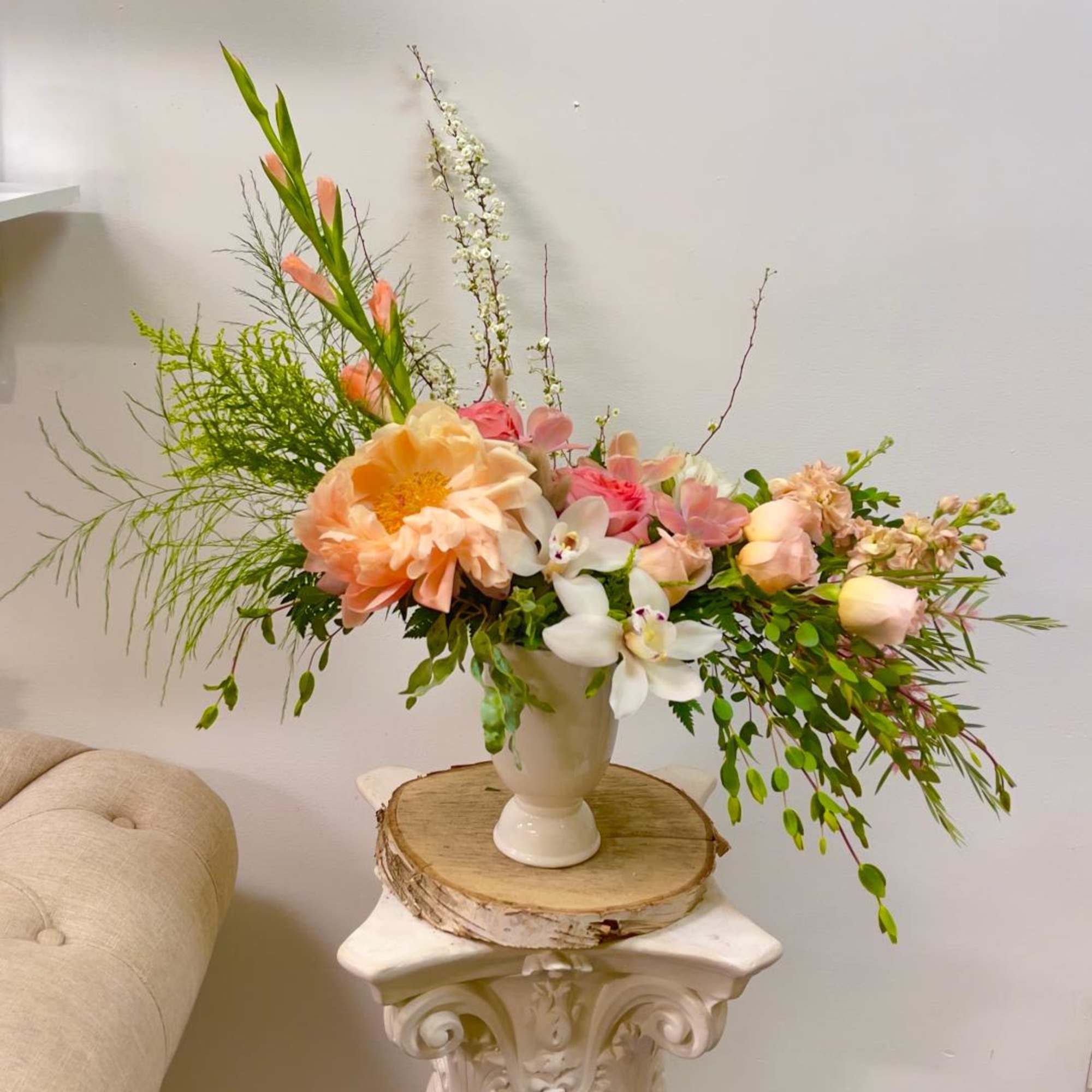 Peach and pink floral arrangement in a white vase on a pedestal