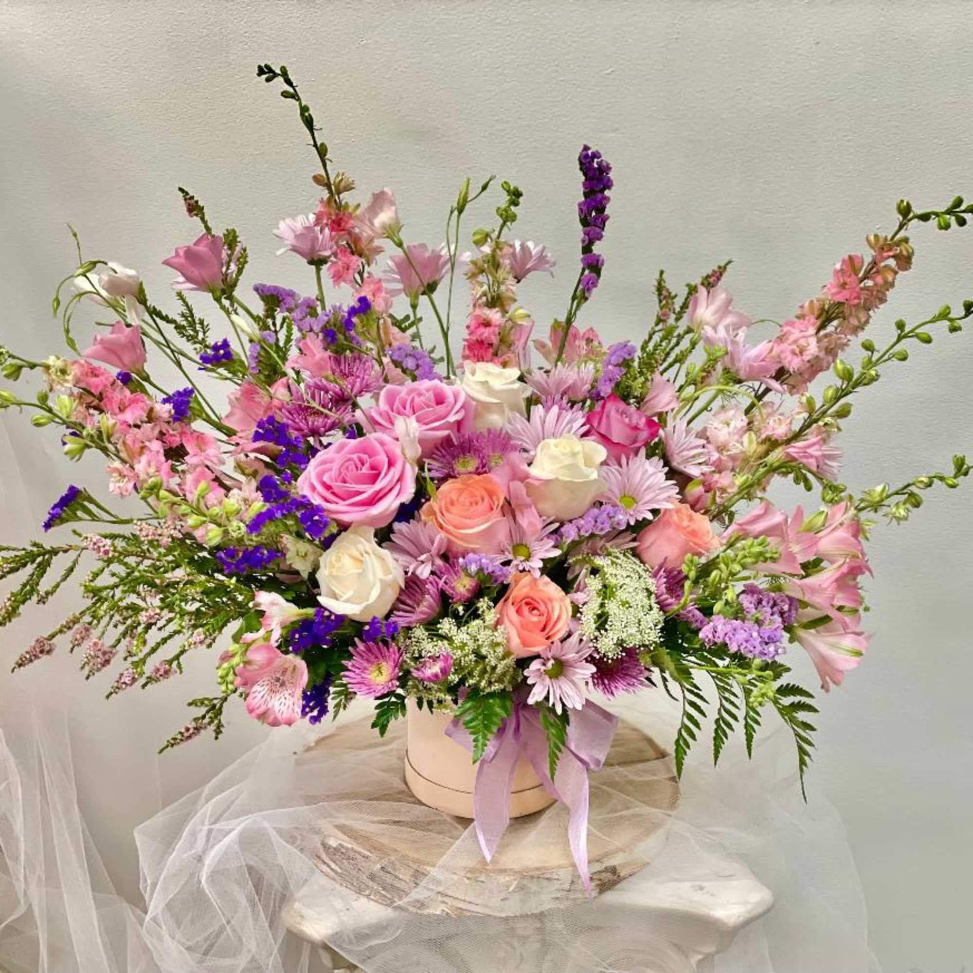 Pink and white mixed flower arrangement in a round box with a lavender ribbon