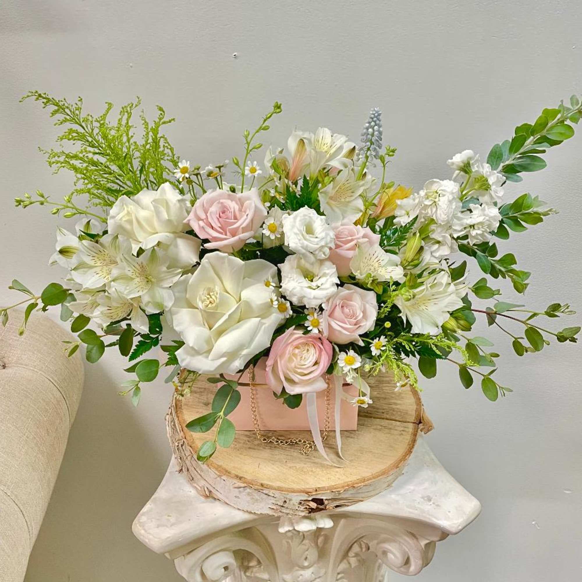 Pink and white floral arrangement in a pink box on a wood slice stand