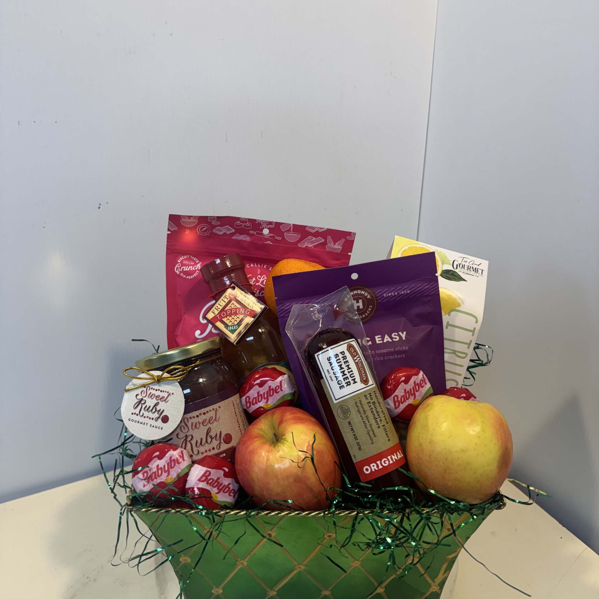 Gift basket with apples, citrus, and packaged snacks in a green container
