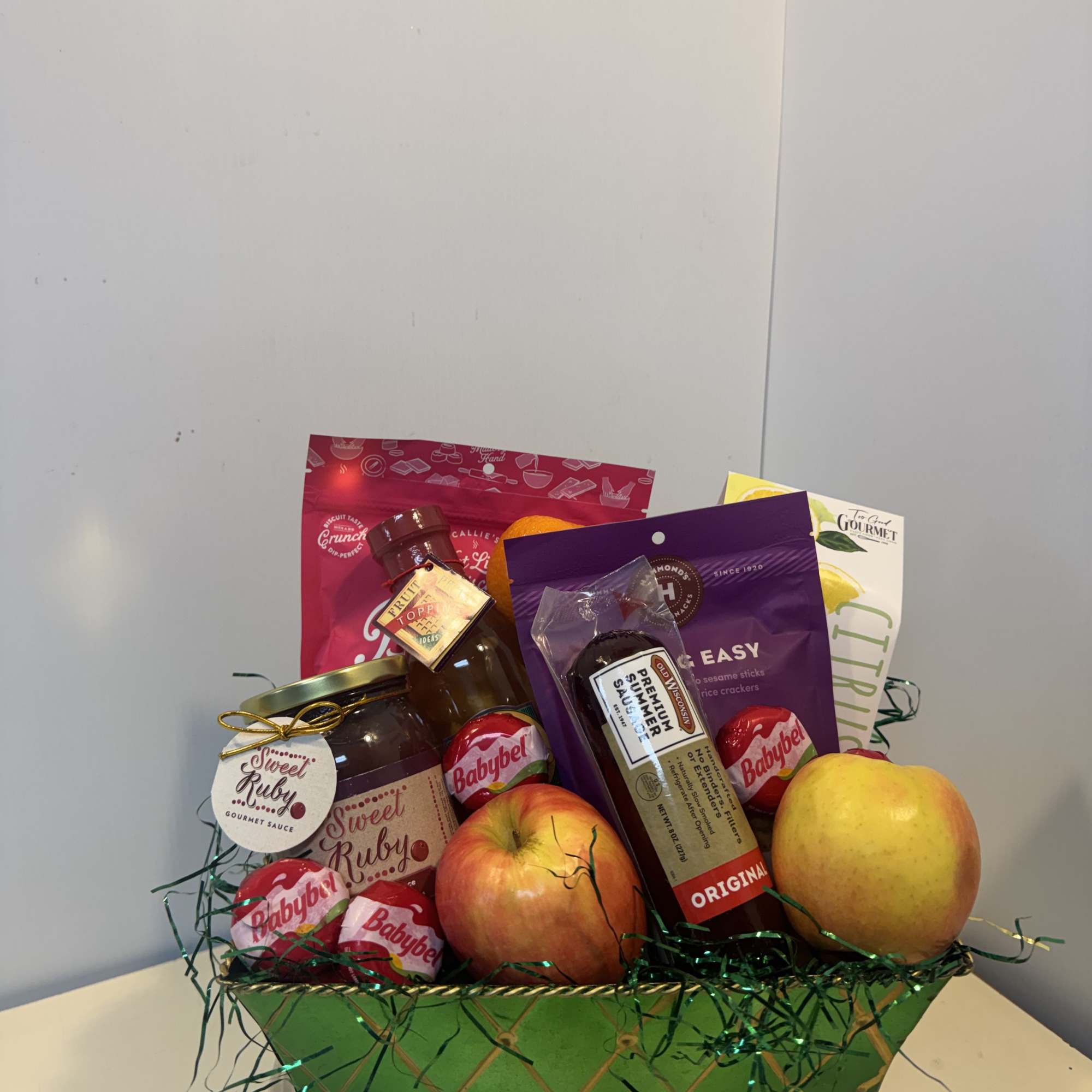 Gift basket with fruit, candy, and snack packages in a green container