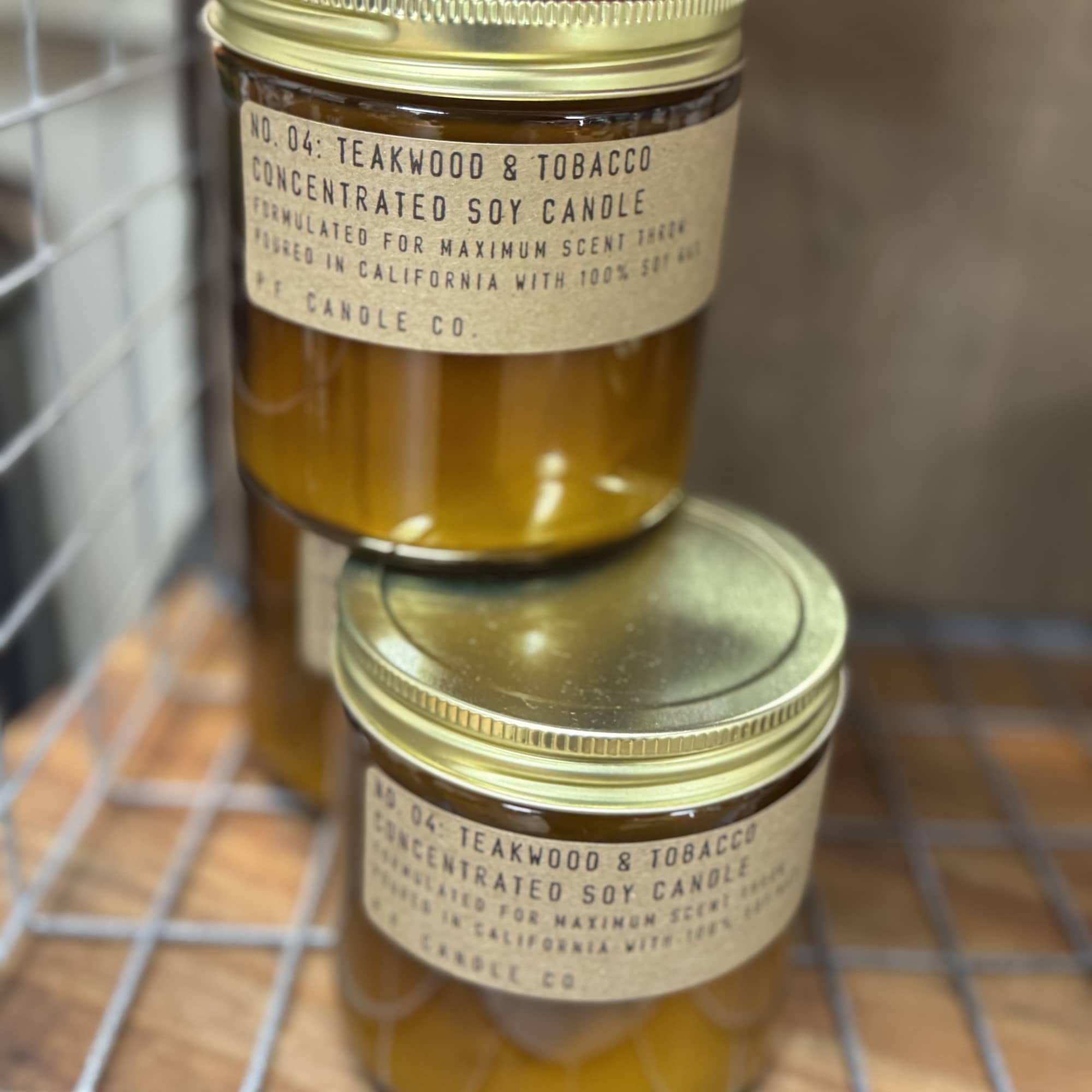 Two amber jar candles with gold lids stacked on a wire rack