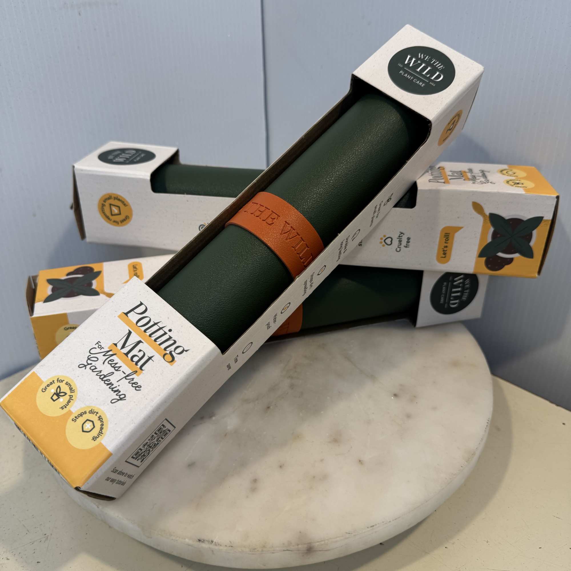 Stacked plant care mats in retail packaging on a round marble stand