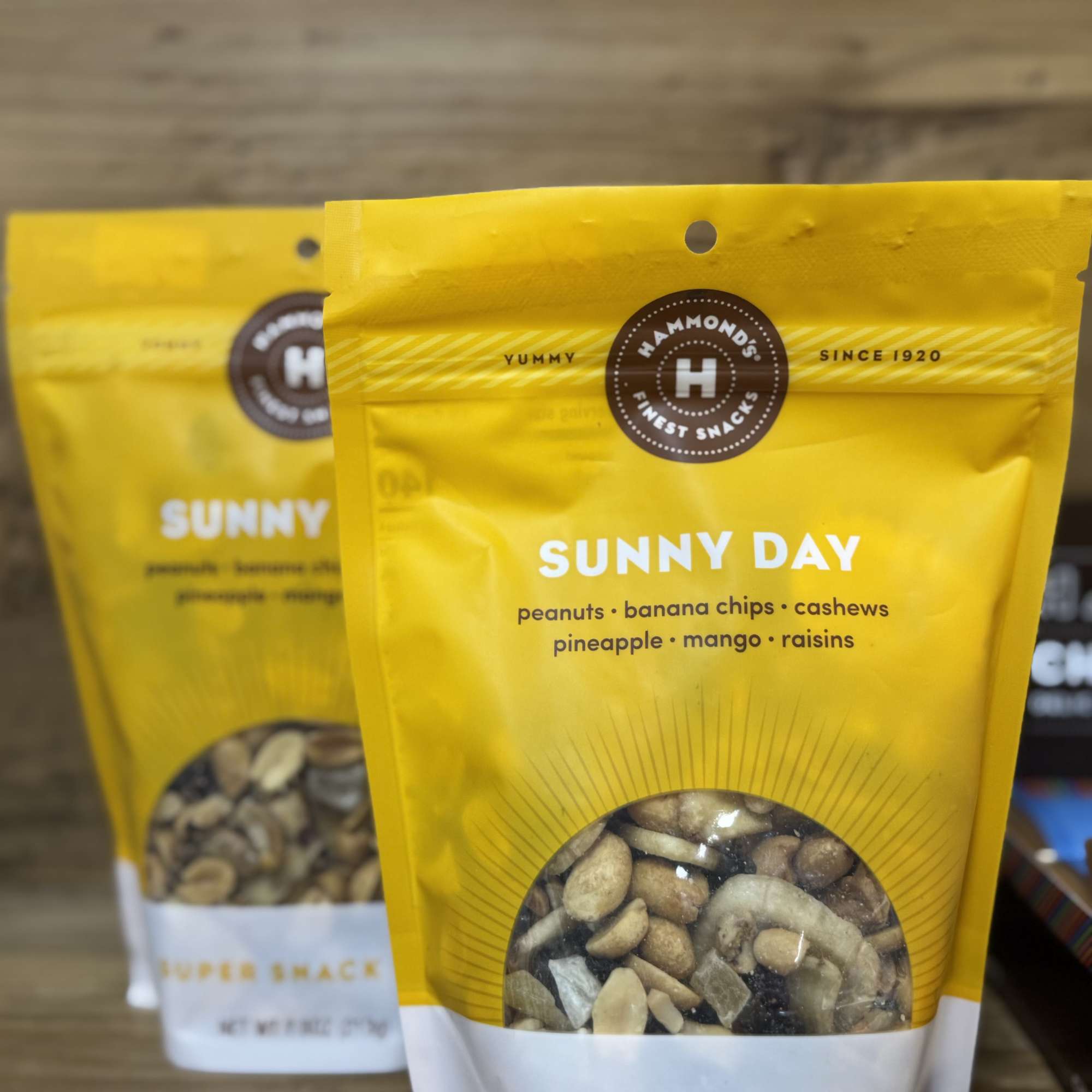 Two yellow snack bags of mixed nuts and dried fruit on a wooden surface.