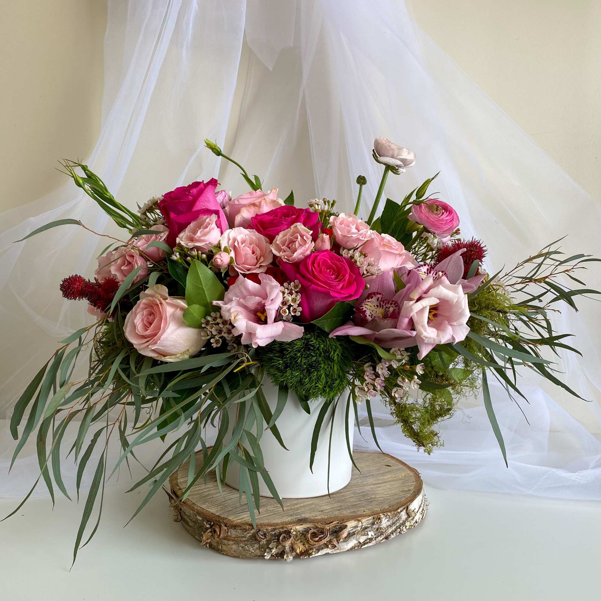 Pink rose bouquet in a white vase with trailing greenery