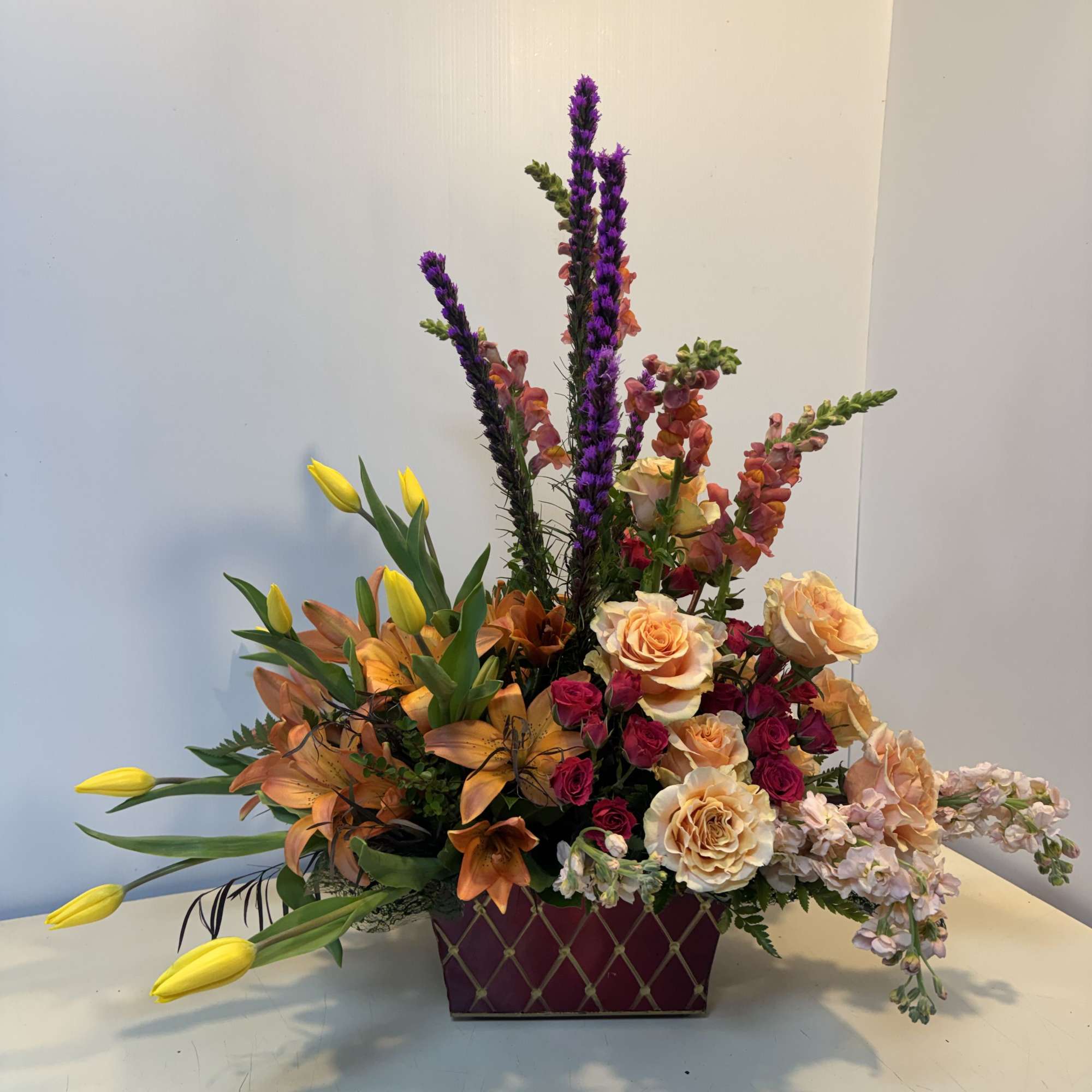 Mixed floral arrangement with roses, lilies, tulips, and purple spikes in a rectangular vase