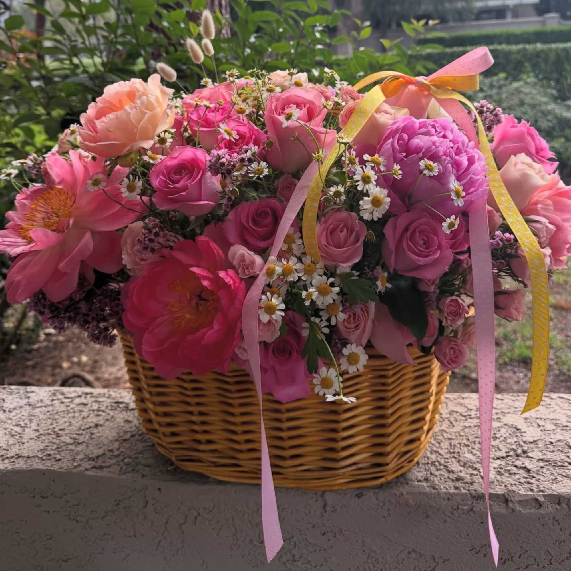 Pink and peach flowers arranged in a wicker basket with ribbon.