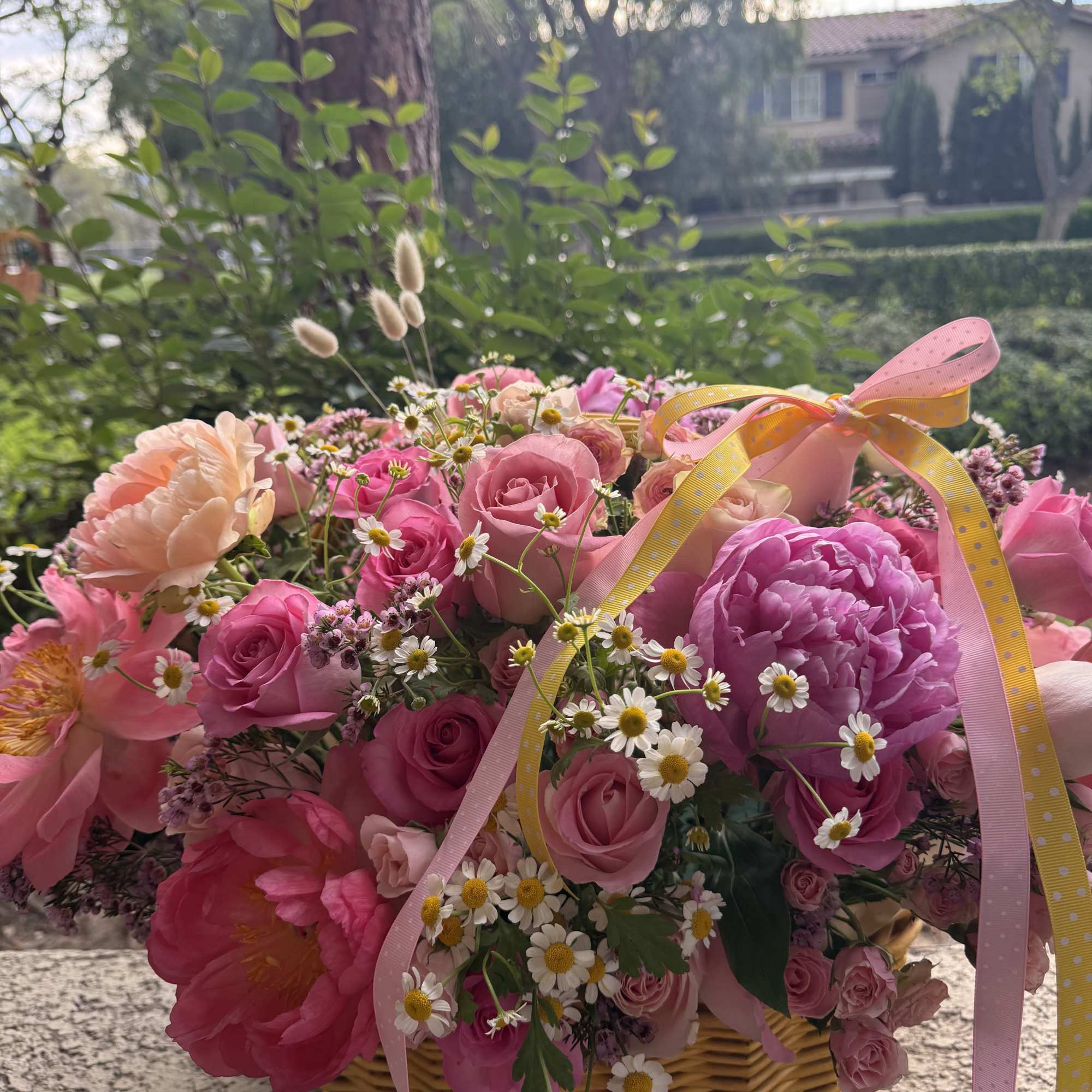 Pink and peach flower arrangement in a wicker basket with ribbon