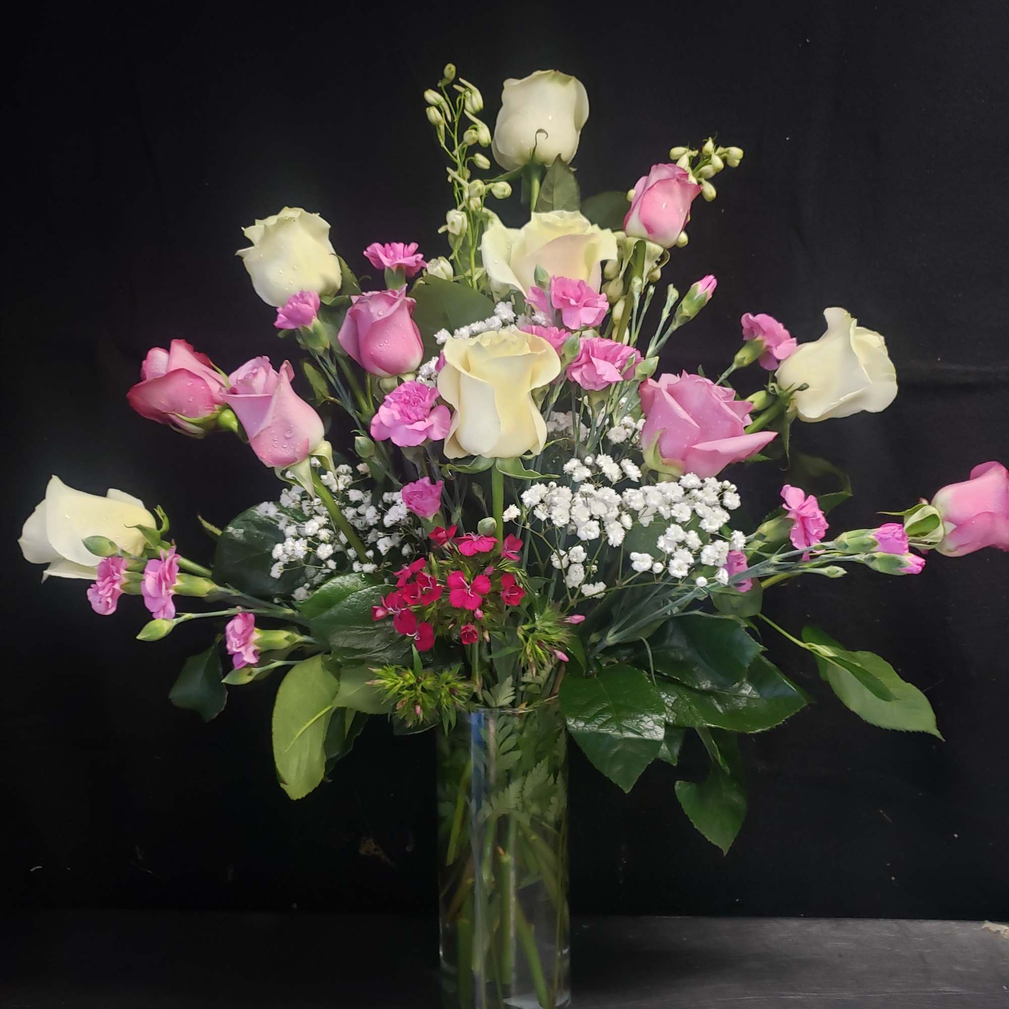 Soft blush and vivid pink roses reach upward in a tall clear