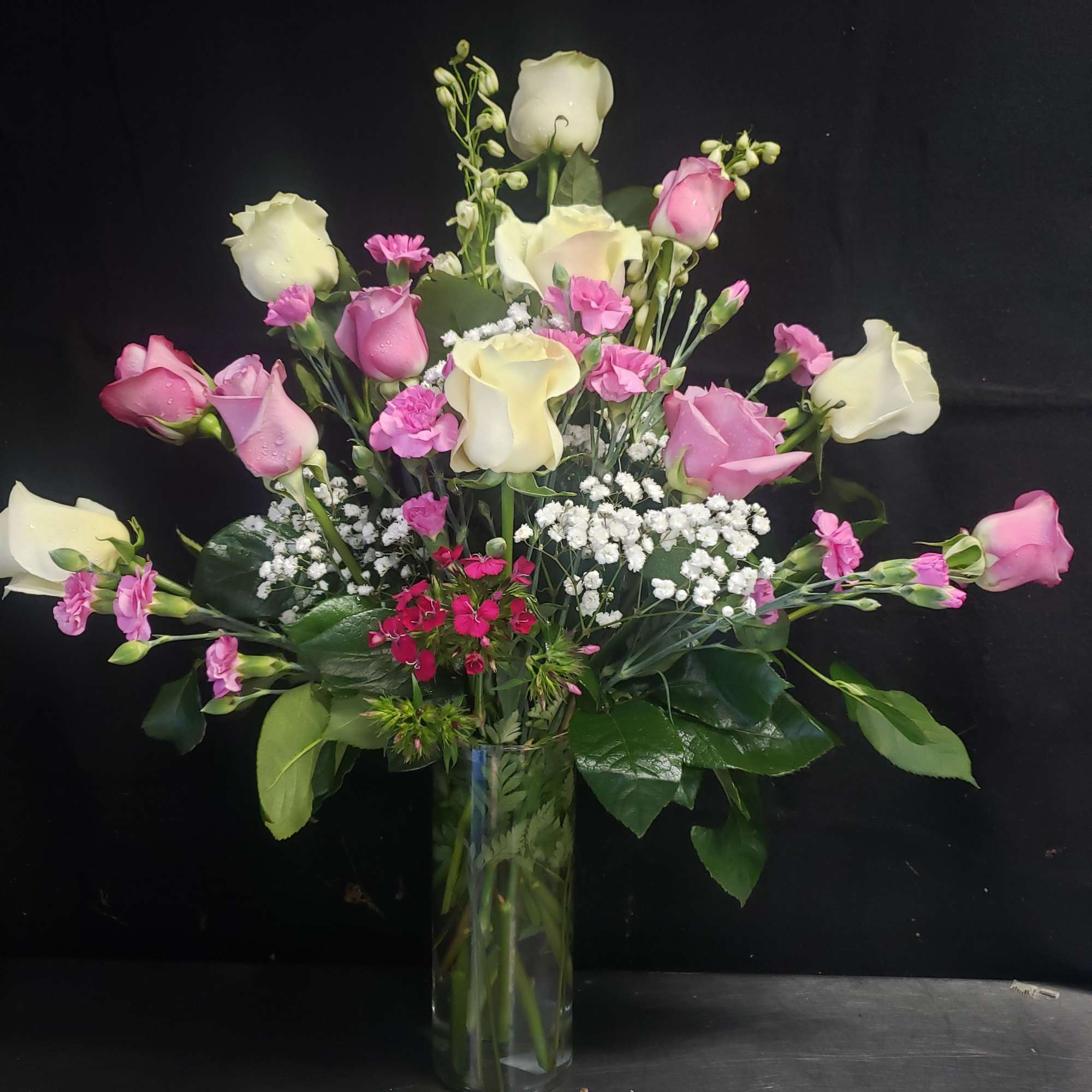 Soft blush and vivid pink roses reach upward in a tall clear