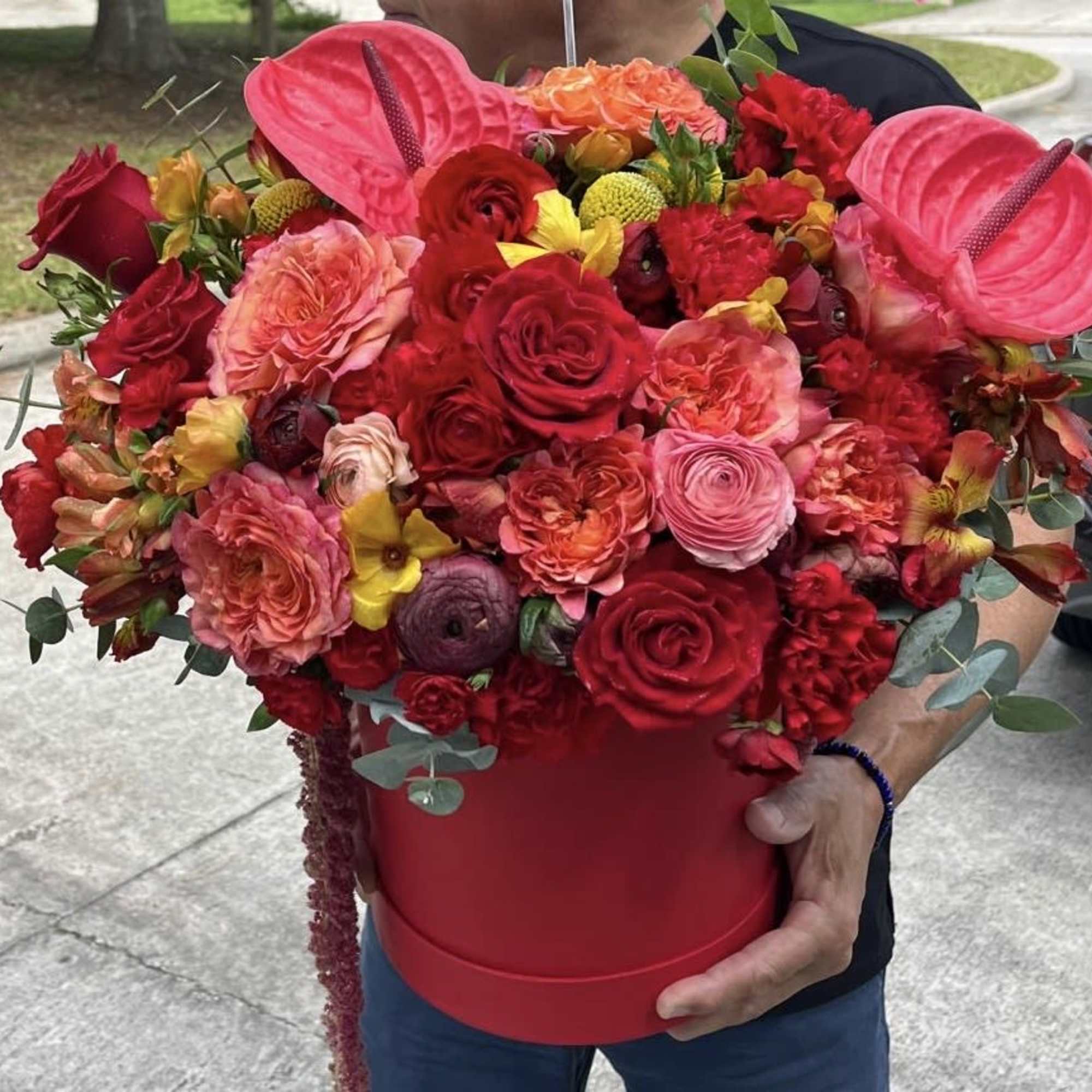 Large red and pink flower arrangement in a red hatbox with anthuriums and roses