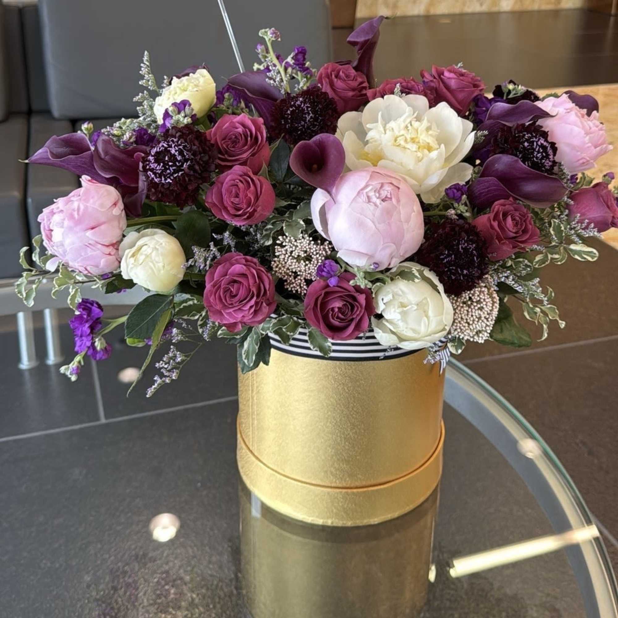 Mixed pink, white, and purple floral arrangement in a gold box
