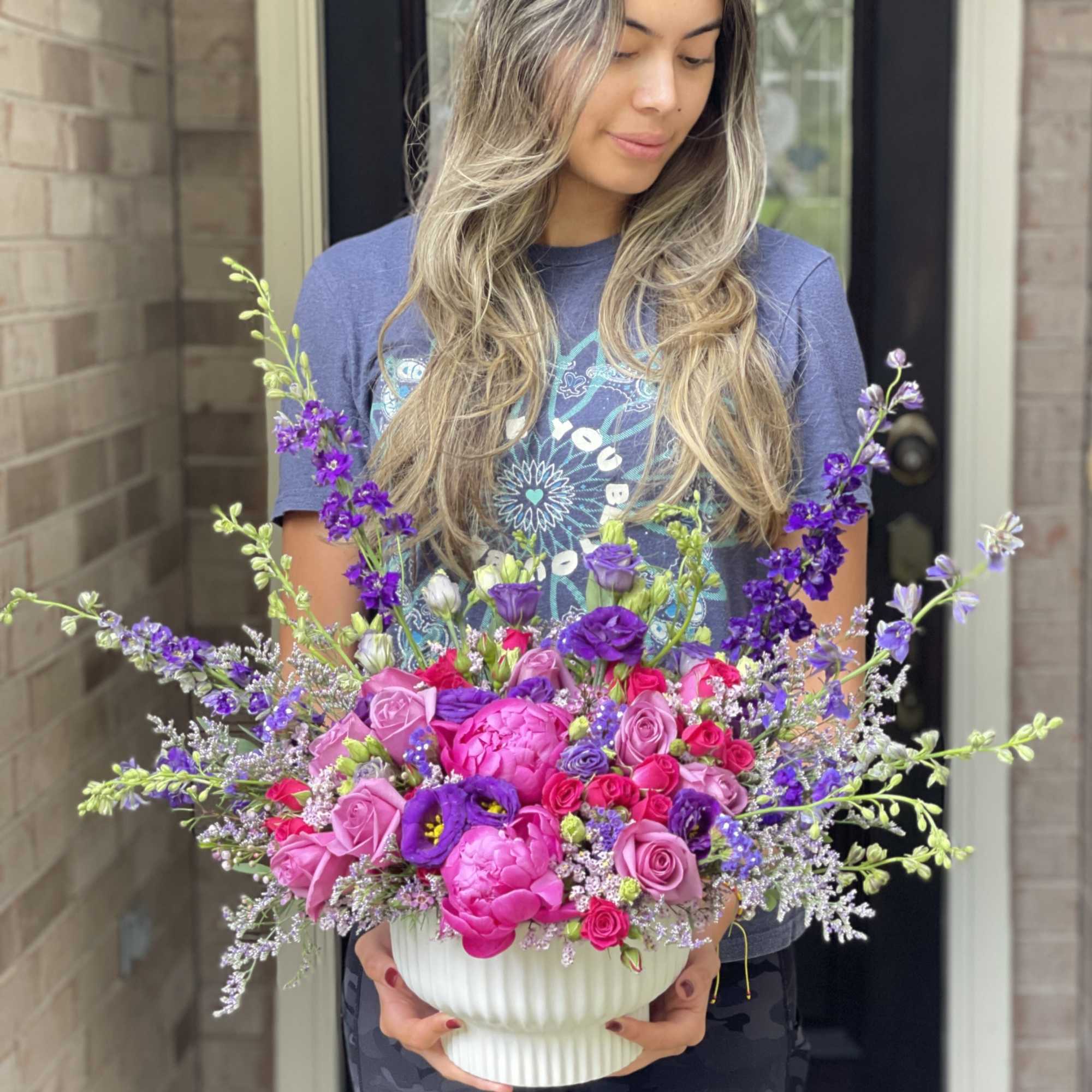 Woman holding a large pink and purple flower arrangement in a white vase