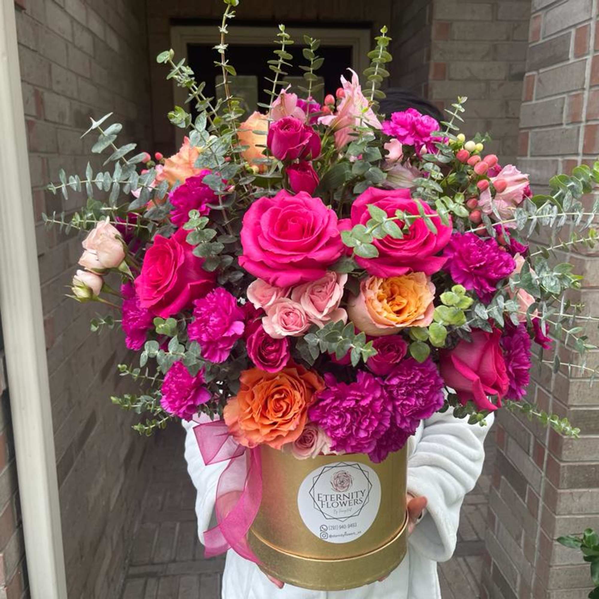 Bright pink and peach roses arranged in a gold hatbox with eucalyptus.