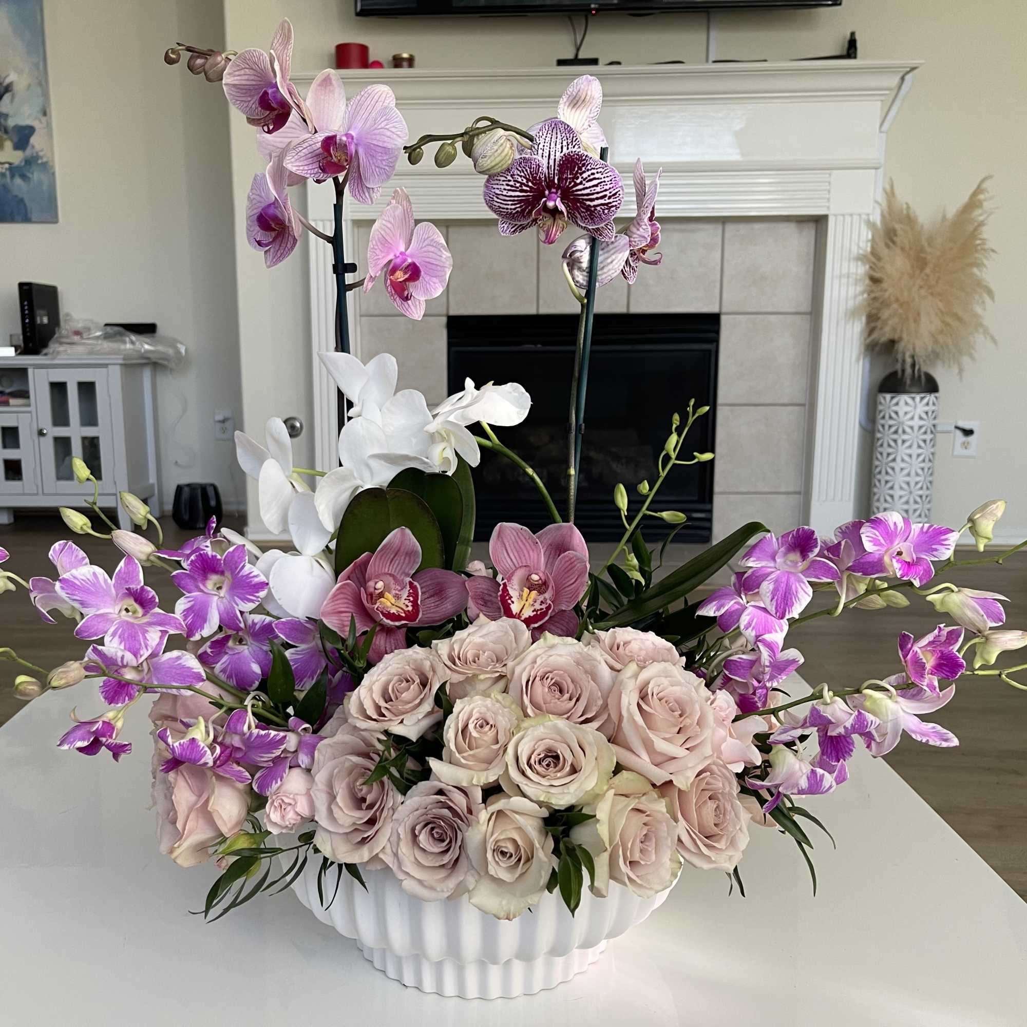 Pink and purple orchids with pale roses in a white vase