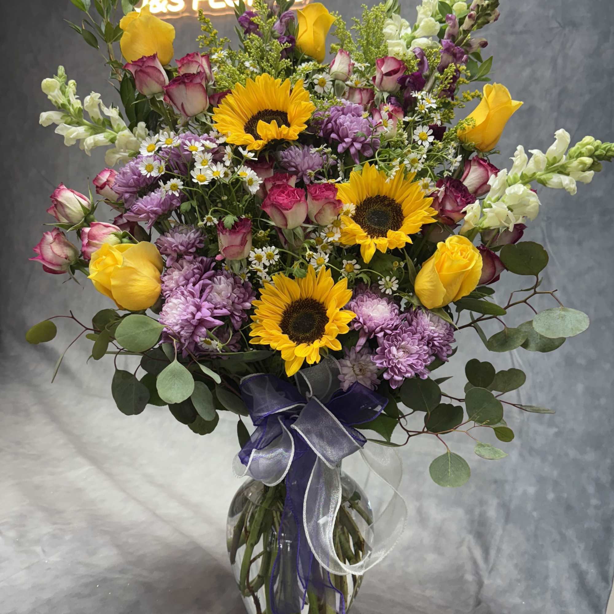 Mixed bouquet of sunflowers, roses, and purple blooms in a glass vase