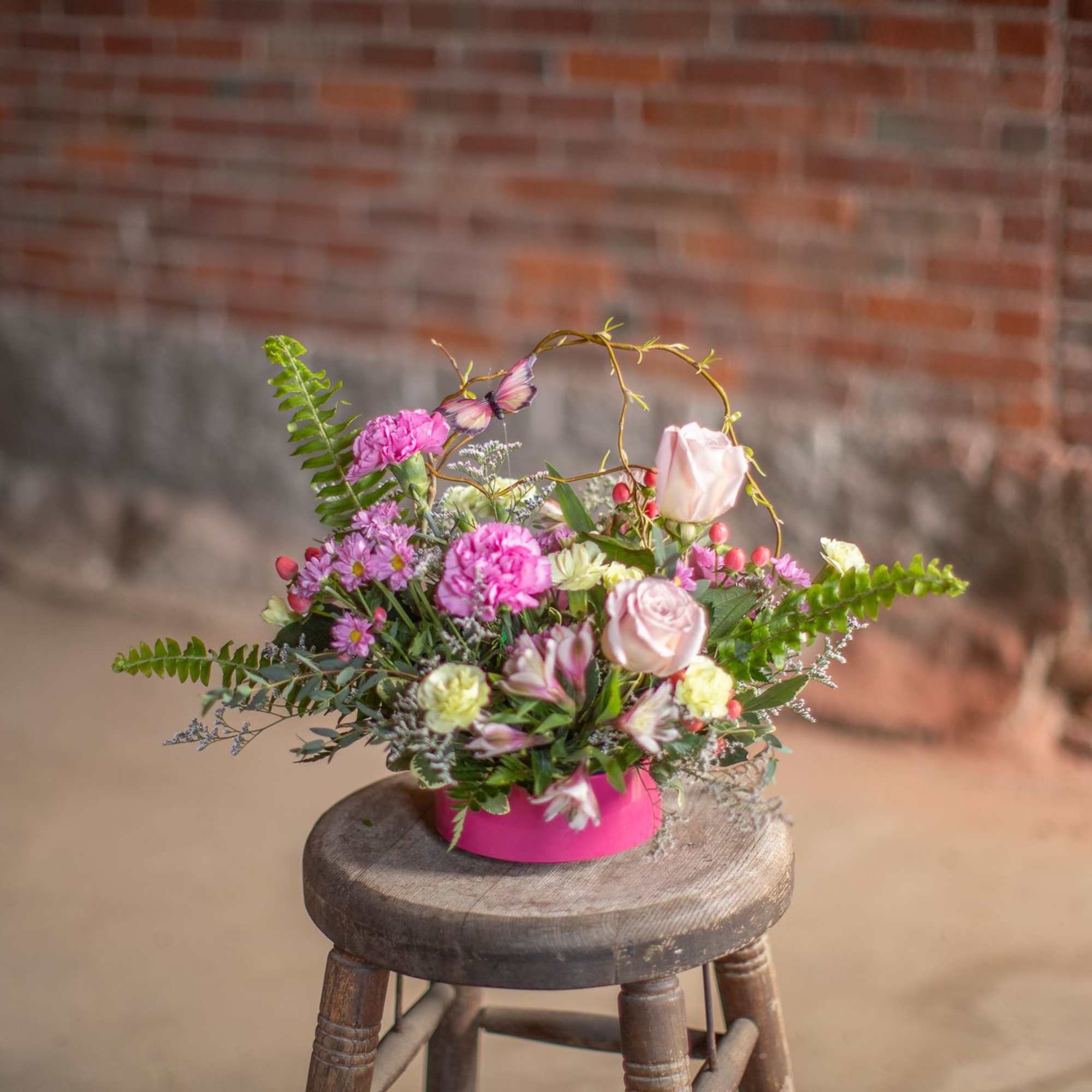 A butterfly dances through woven curly willow branches and festive seasonal blooms